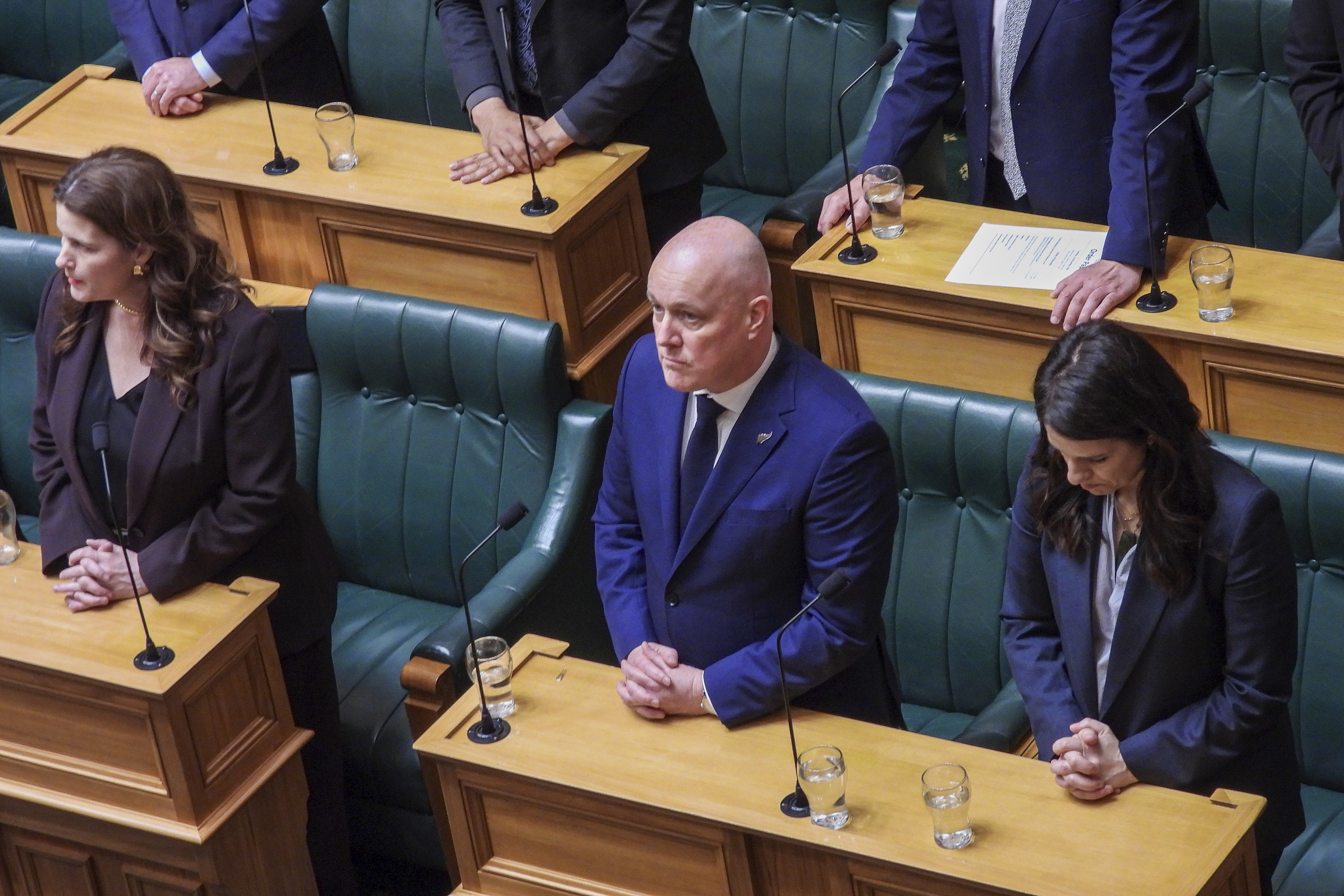 New Zealand Prime Minister Christopher Luxon, center, stands in silence ahead of making a "formal and unreserved" apology in Parliament for the widespread abuse, torture and neglect of hundreds of thousands of children and vulnerable adults in care, in Wellington, New Zealand Tuesday, Nov. 12, 2024. (AP Photo/Charlotte Graham-McLay )