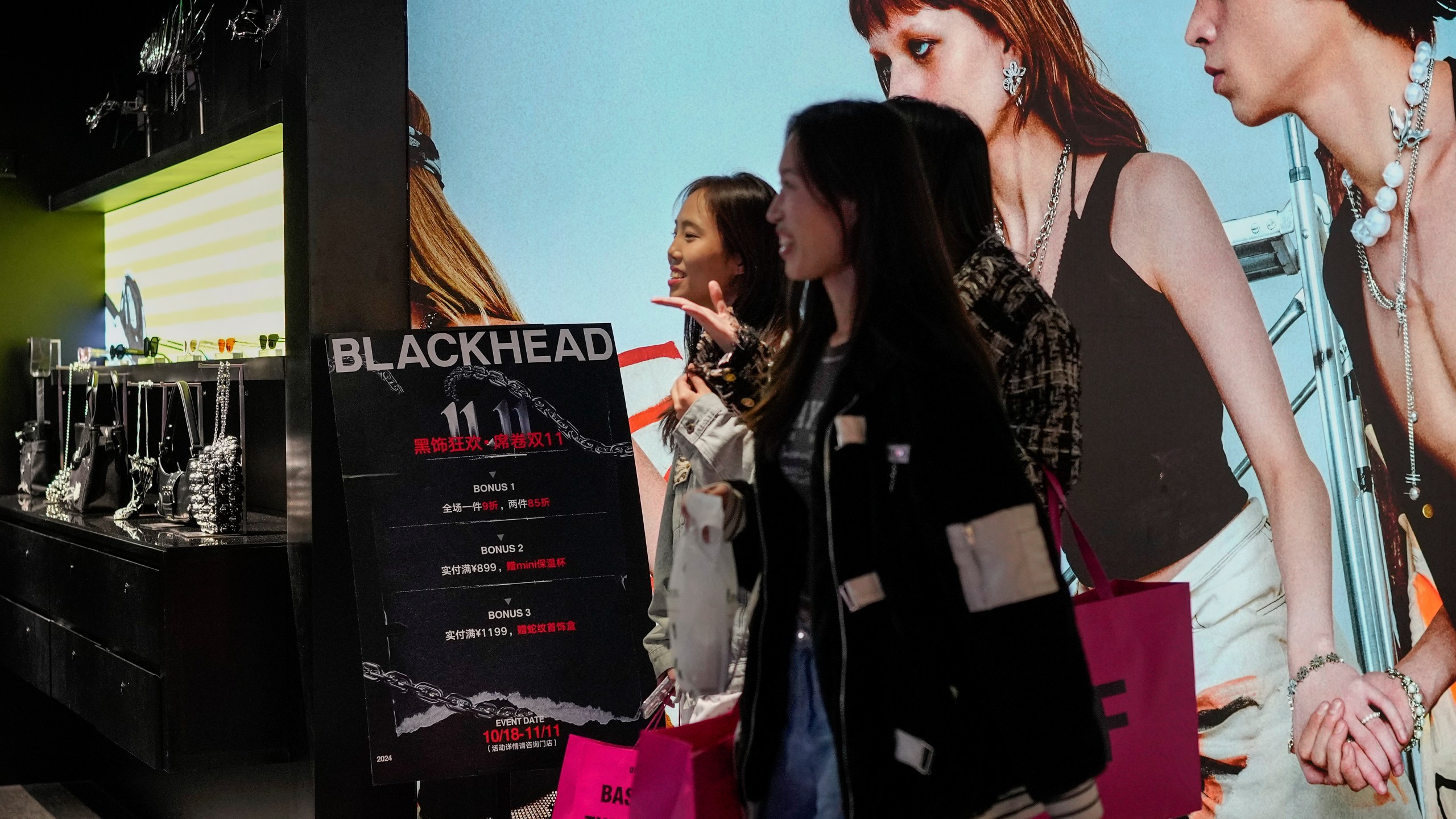 Women walk at a fashion accessories store displaying a poster to promote Singles' Day discounts at a shopping mall in Beijing, Monday, Nov. 11, 2024. (AP Photo/Andy Wong)