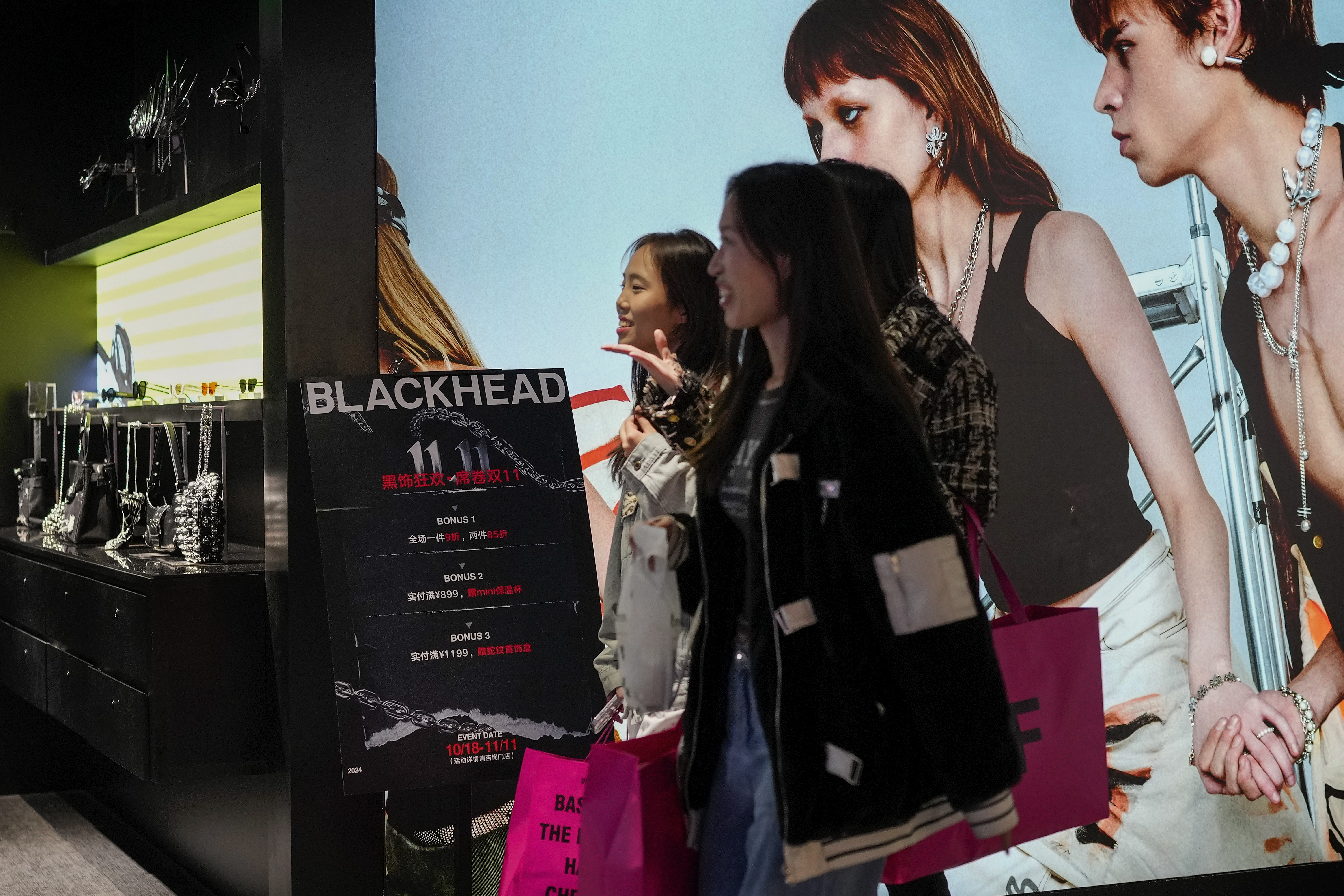 Women walk at a fashion accessories store displaying a poster to promote Singles' Day discounts at a shopping mall in Beijing, Monday, Nov. 11, 2024. (AP Photo/Andy Wong)