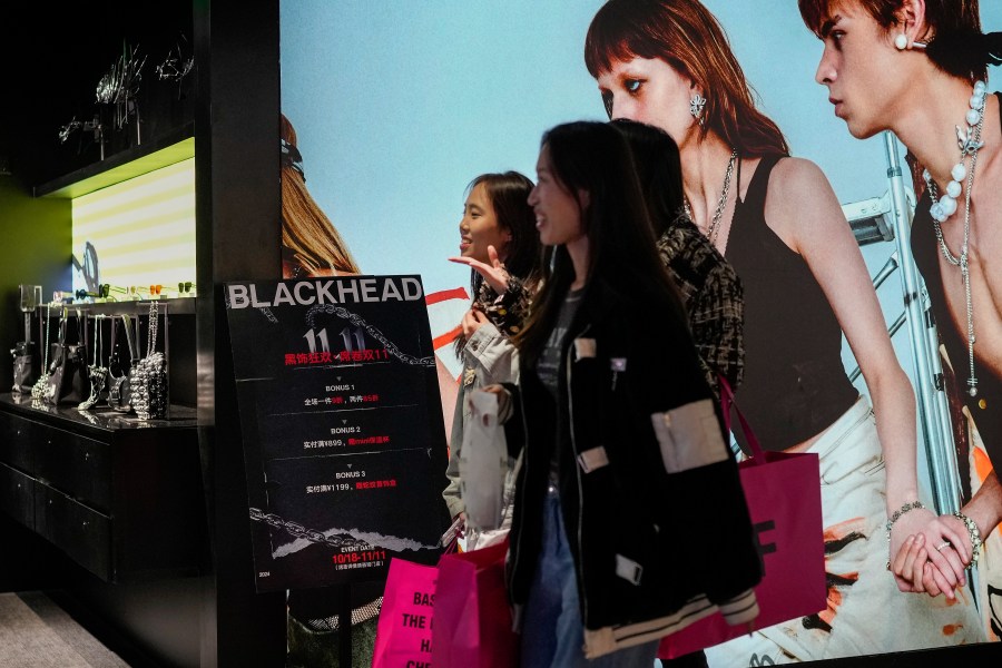 Women walk at a fashion accessories store displaying a poster to promote Singles' Day discounts at a shopping mall in Beijing, Monday, Nov. 11, 2024. (AP Photo/Andy Wong)