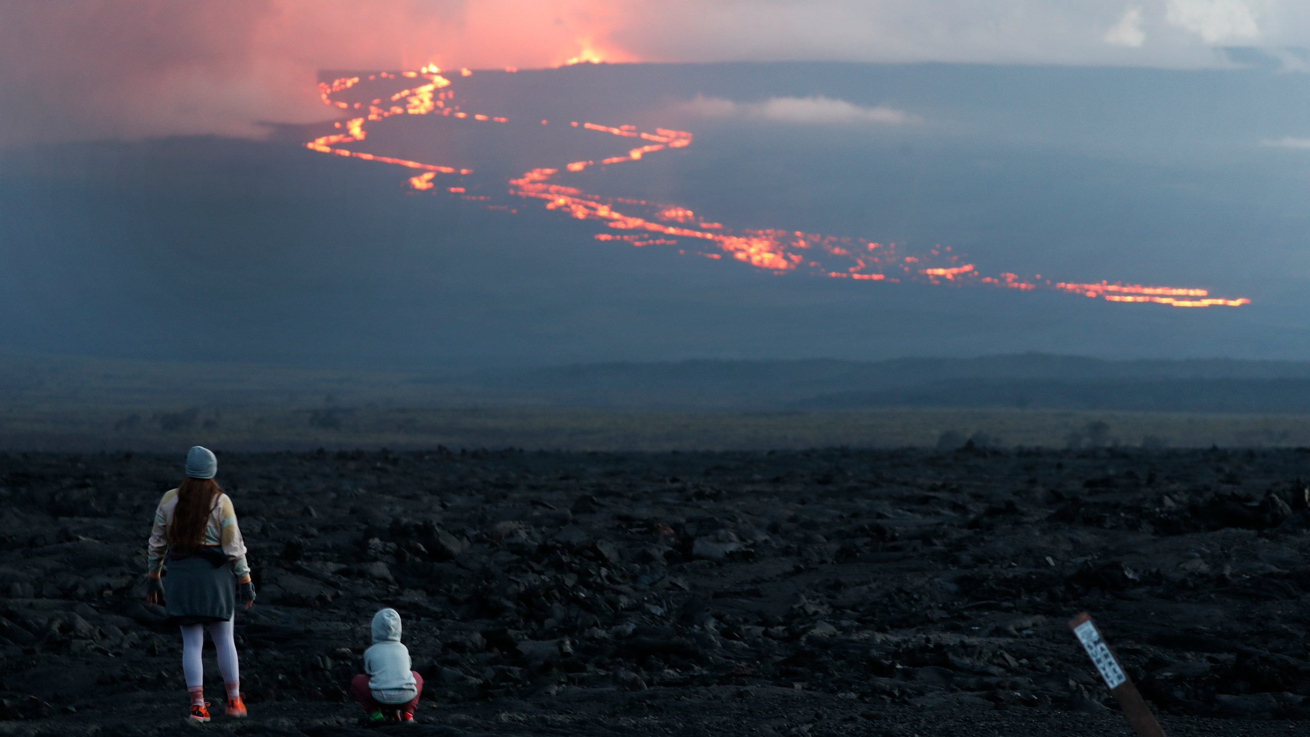 FILE - Spectators watch the lava flow down the mountain from the Mauna Loa eruption, Tuesday, Nov. 29, 2022, near Hilo, Hawaii. (AP Photo/Marco Garcia, File)