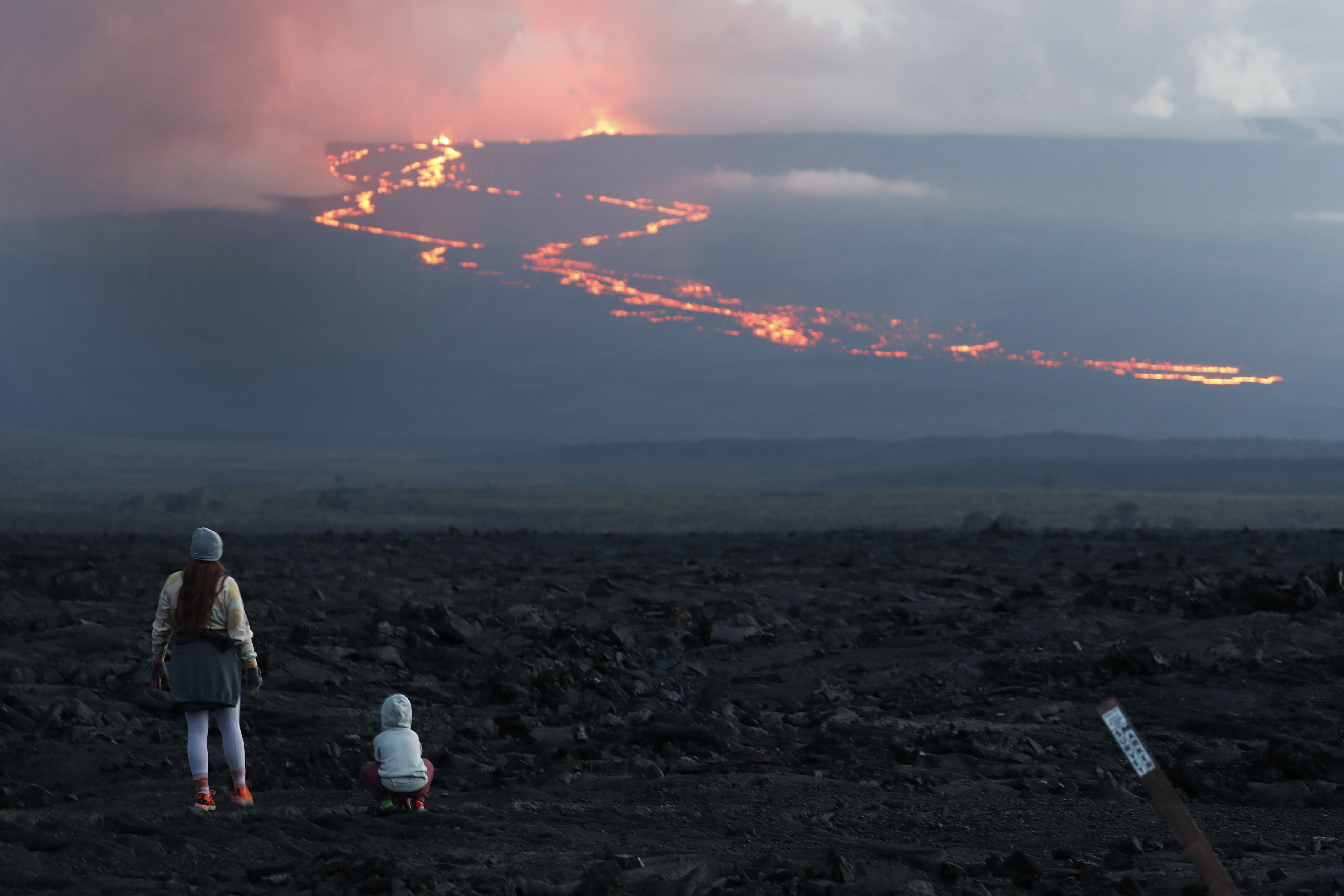 FILE - Spectators watch the lava flow down the mountain from the Mauna Loa eruption, Tuesday, Nov. 29, 2022, near Hilo, Hawaii. (AP Photo/Marco Garcia, File)