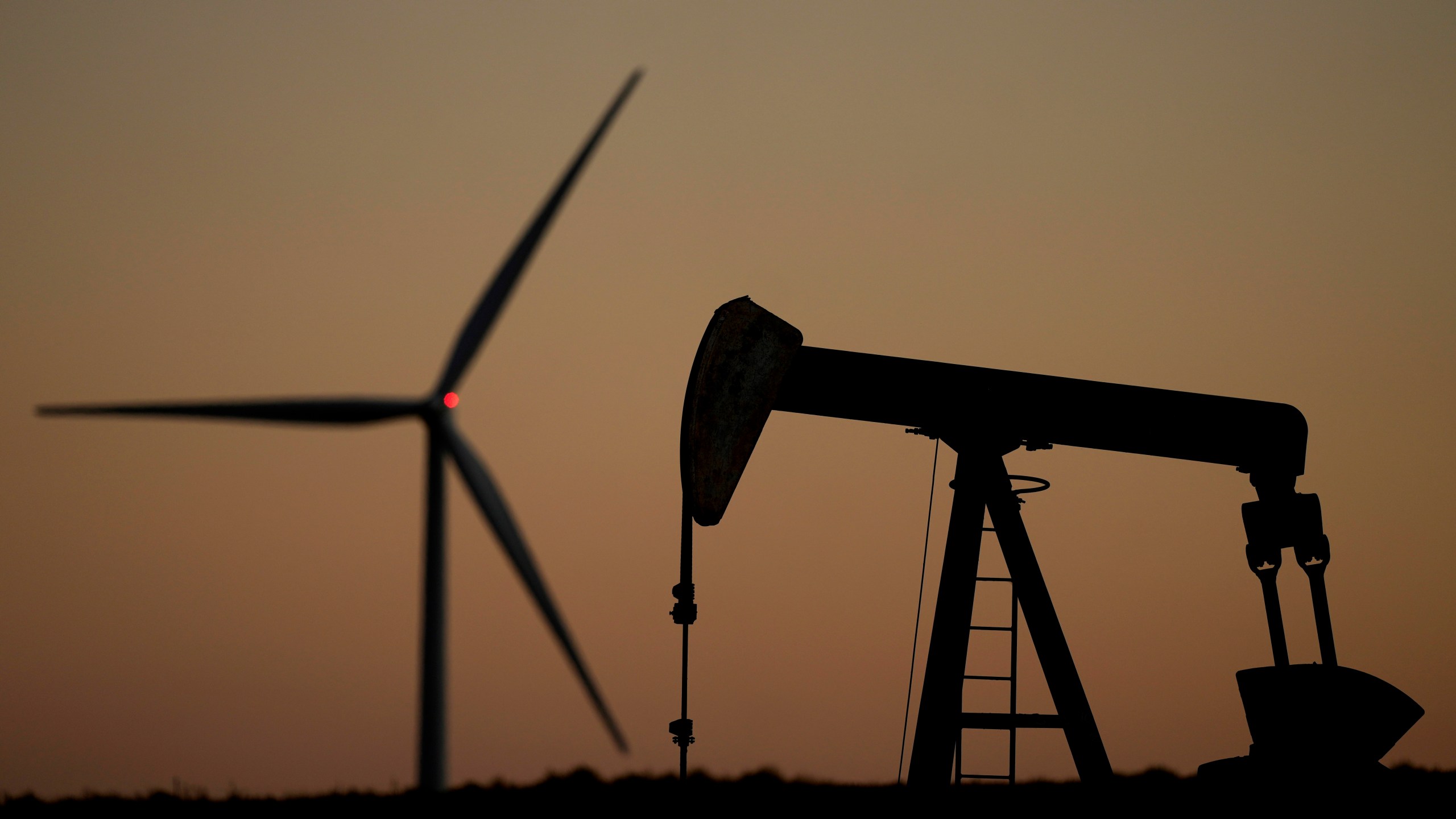 A pumpjack operates in the foreground while a wind turbine at the Buckeye Wind Energy wind farm rises in the distance, Monday, Sept. 30, 2024, near Hays, Kan. (AP Photo/Charlie Riedel)