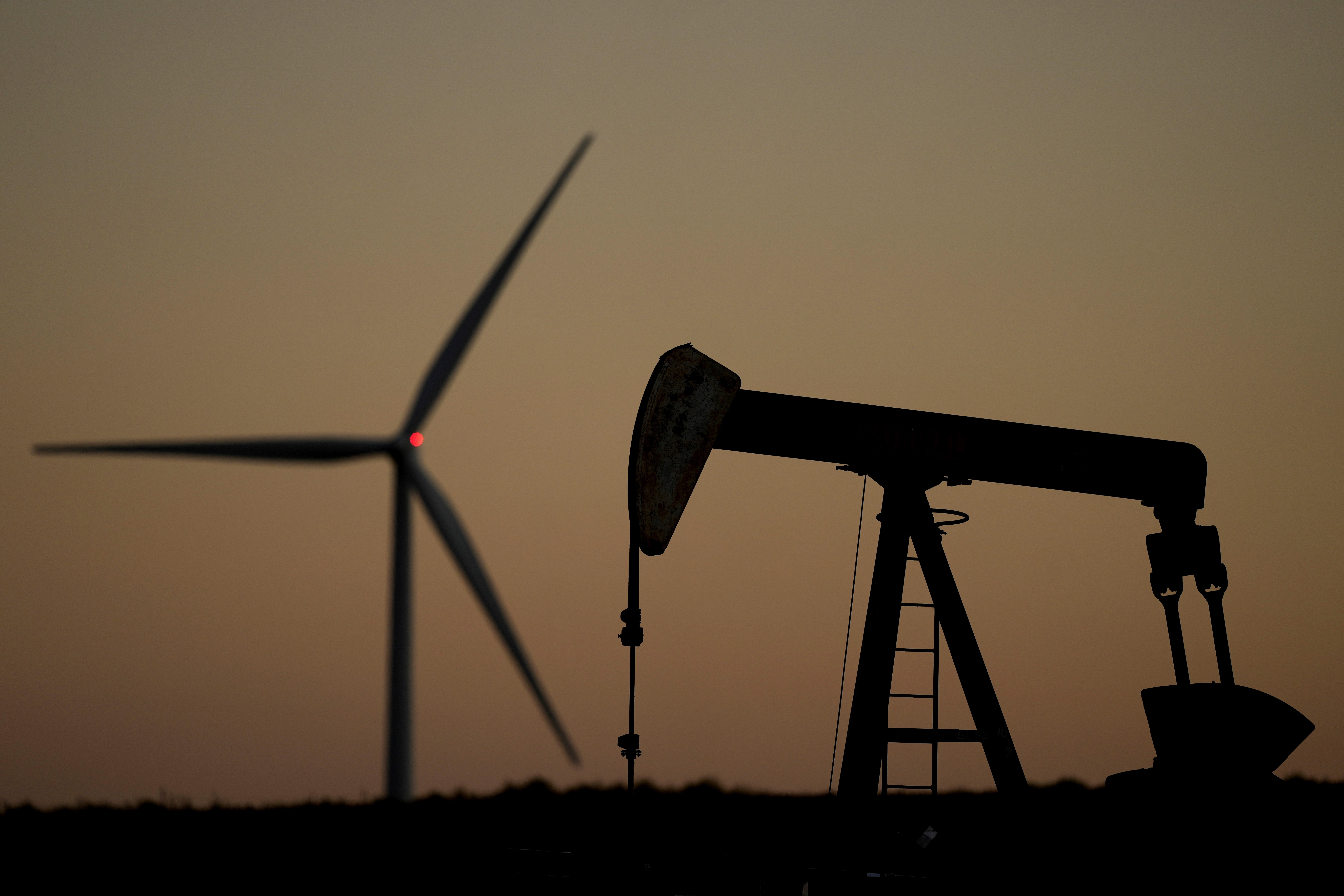 A pumpjack operates in the foreground while a wind turbine at the Buckeye Wind Energy wind farm rises in the distance, Monday, Sept. 30, 2024, near Hays, Kan. (AP Photo/Charlie Riedel)