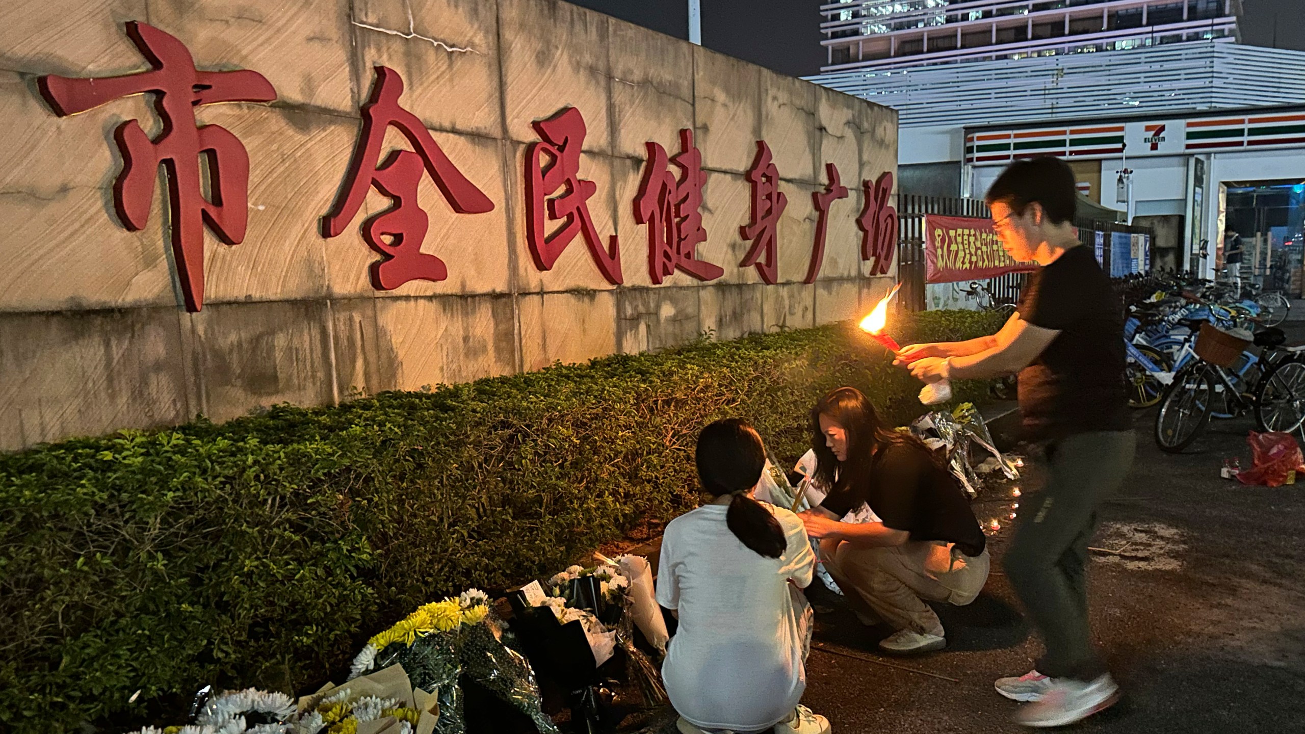 A woman lights a candle as offering near flowers placed outside the "Zhuhai People's Fitness Plaza" where a man deliberately rammed his car into people exercising at the sports center, killing some and injuring others in Zhuhai in southern China's Guangdong province on Tuesday, Nov. 12, 2024. (AP Photo/Ng Han Guan)