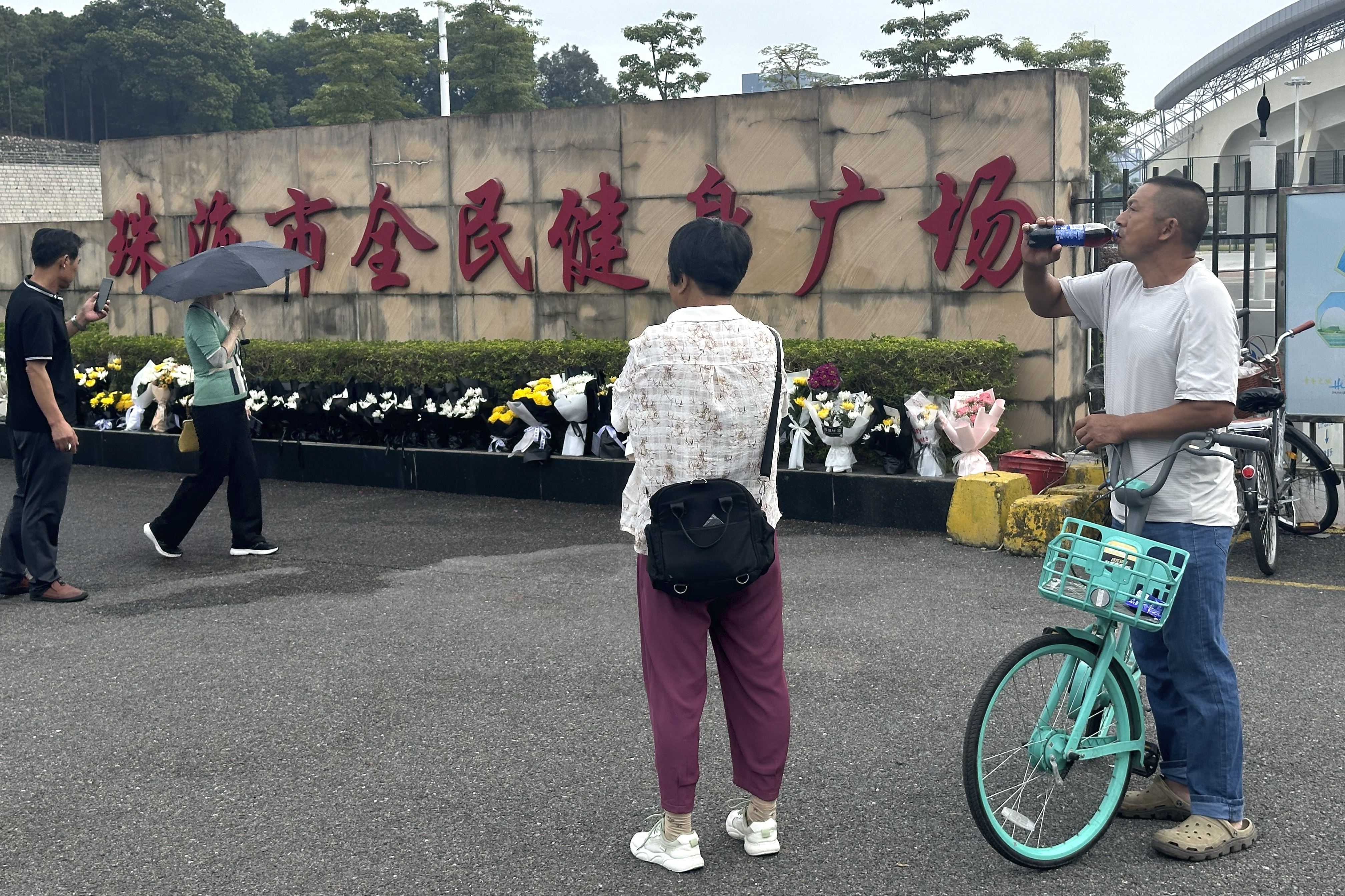 Residents look at flowers laid outside the "Zhuhai People's Fitness Plaza" where a man rammed his car into people exercising at the sports center, in Zhuhai in southern China's Guangdong province on Wednesday, Nov. 13, 2024. (AP Photo/Ng Han Guan)