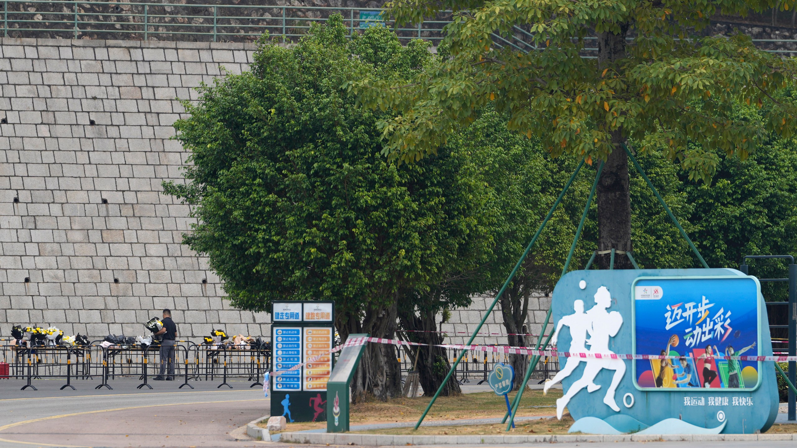 Volunteers relocate flowers laid outside "Zhuhai People's Fitness Plaza" to a barrier leading into the area where a man rammed his car into people exercising at the sports center, in Zhuhai in southern China's Guangdong province on Wednesday, Nov. 13, 2024. (AP Photo/Ng Han Guan)