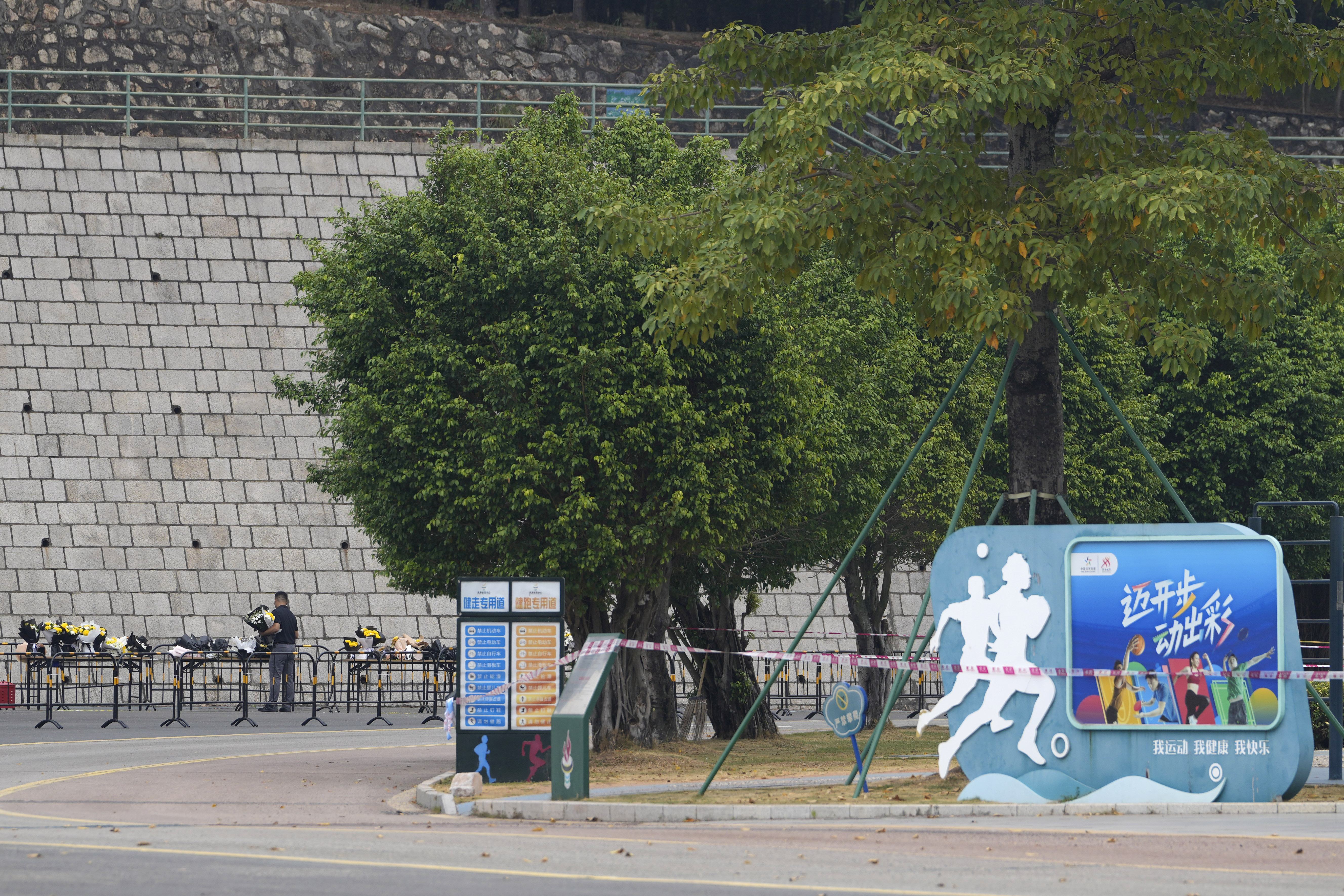 Volunteers relocate flowers laid outside "Zhuhai People's Fitness Plaza" to a barrier leading into the area where a man rammed his car into people exercising at the sports center, in Zhuhai in southern China's Guangdong province on Wednesday, Nov. 13, 2024. (AP Photo/Ng Han Guan)