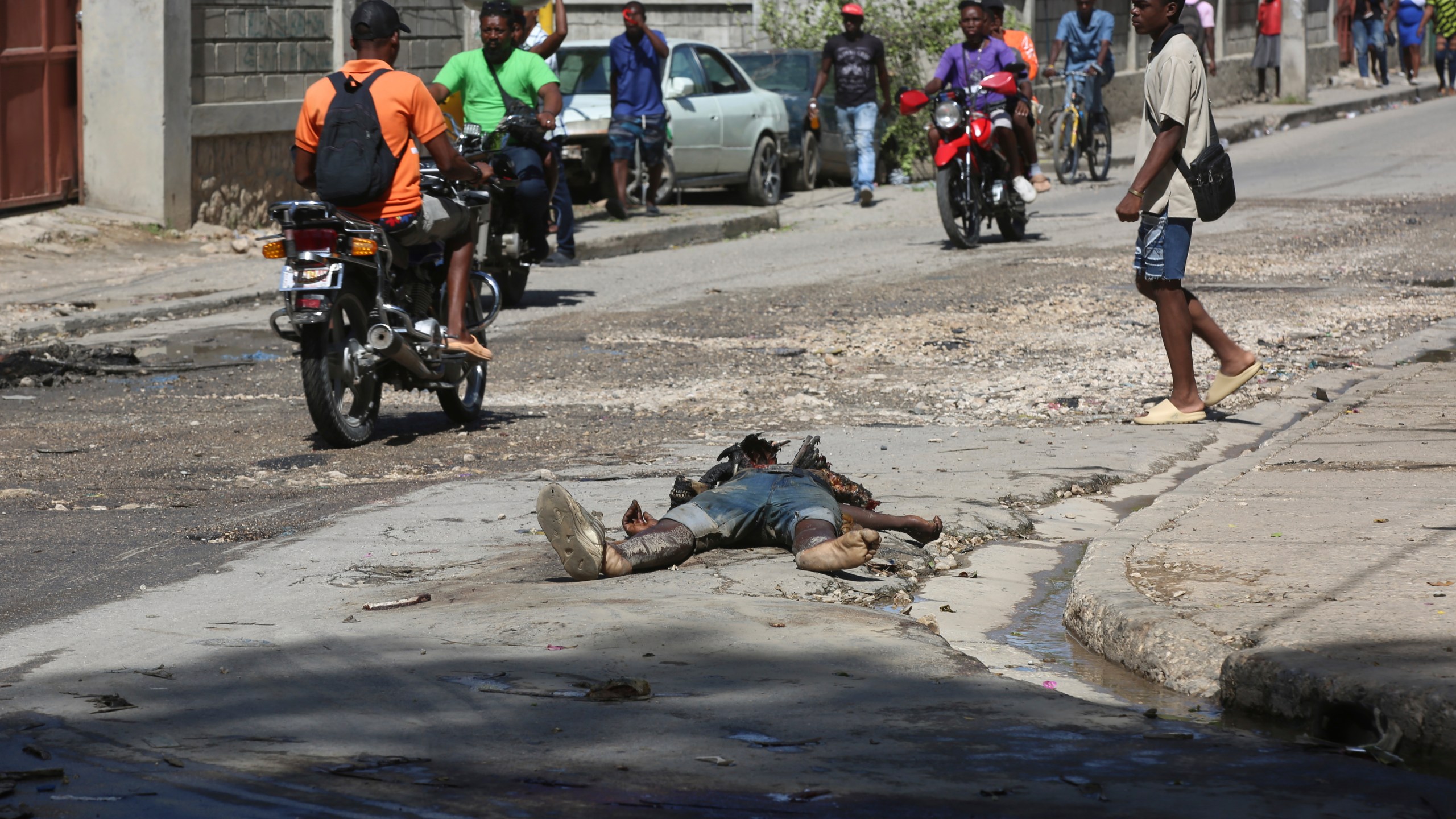 Pedestrians walk past the decomposing body of a man left abandoned on a street in downtown Port-au-Prince, Haiti, Wednesday, Nov. 13, 2024. (AP Photo/Odelyn Joseph)