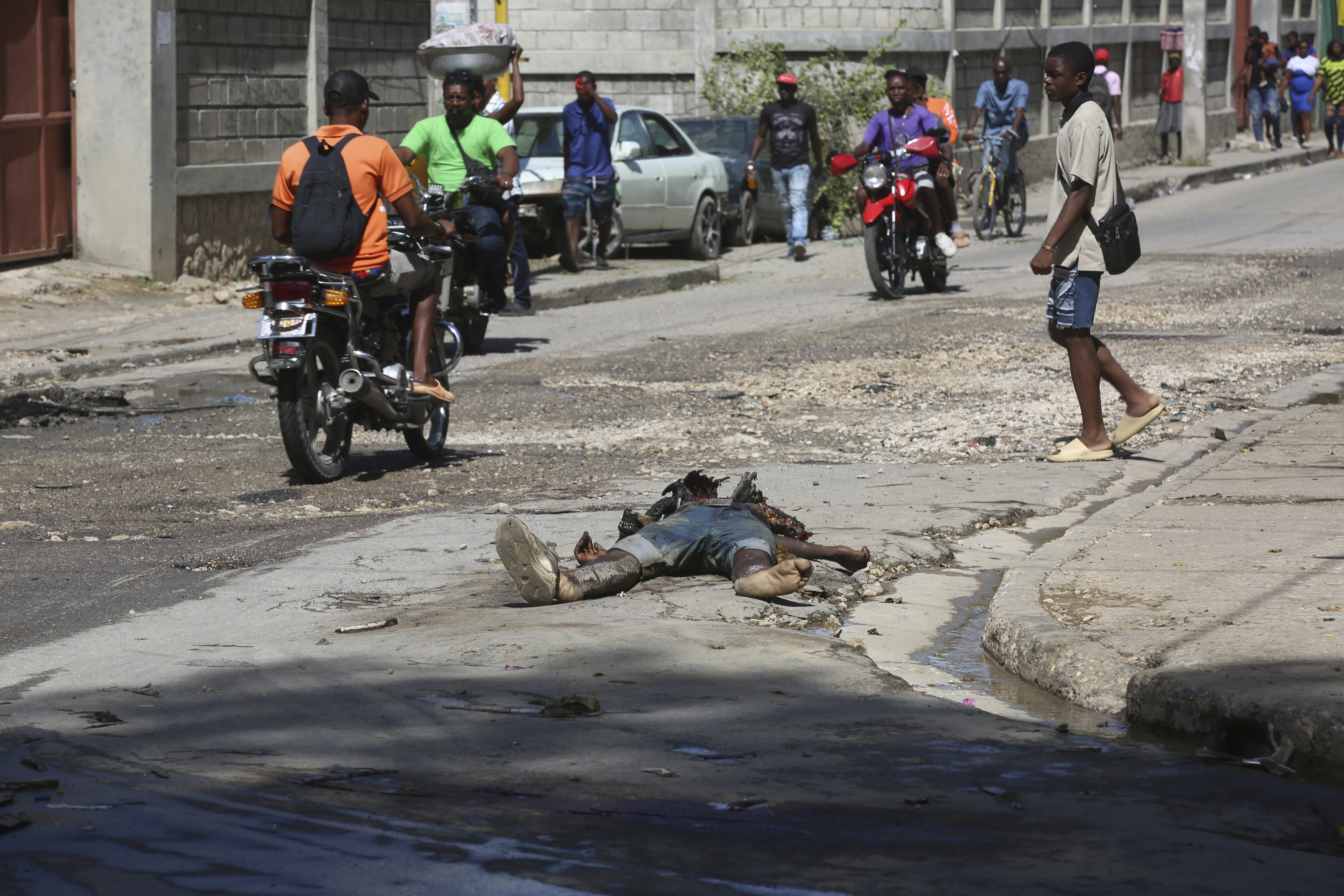 Pedestrians walk past the decomposing body of a man left abandoned on a street in downtown Port-au-Prince, Haiti, Wednesday, Nov. 13, 2024. (AP Photo/Odelyn Joseph)