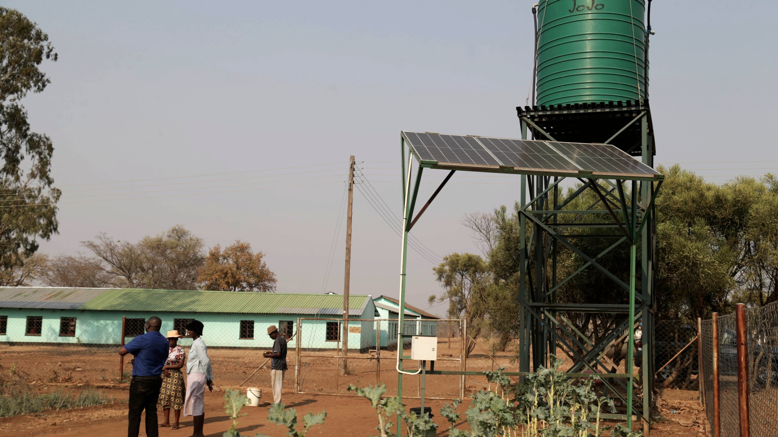 Villagers stand next to solar panels and water tanks that are part of a climate-smart agriculture program funded by the United States Agency for International Development in Chipinge, Zimbabwe on Thursday, Sept. 19, 2024. (AP Photo/Aaron Ufumeli)