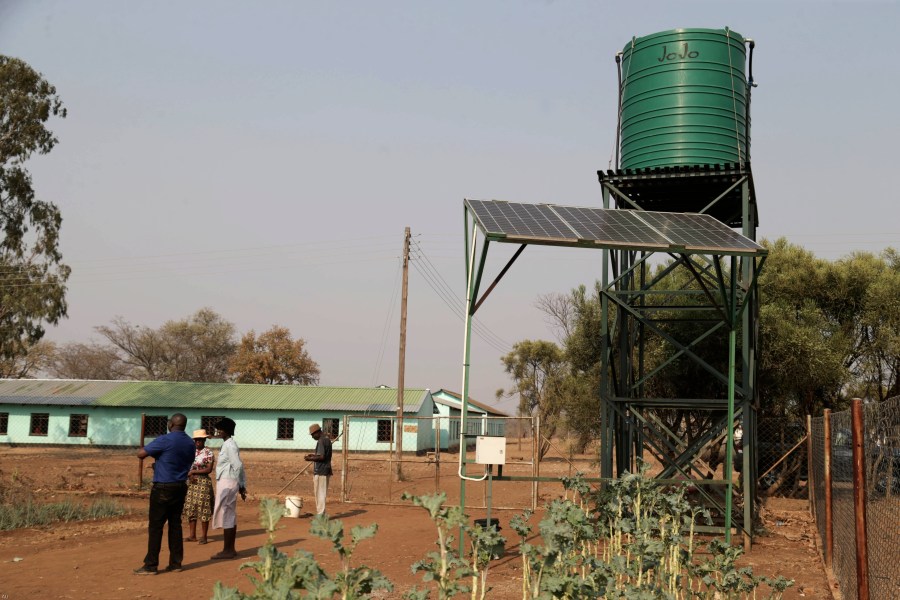 Villagers stand next to solar panels and water tanks that are part of a climate-smart agriculture program funded by the United States Agency for International Development in Chipinge, Zimbabwe on Thursday, Sept. 19, 2024. (AP Photo/Aaron Ufumeli)