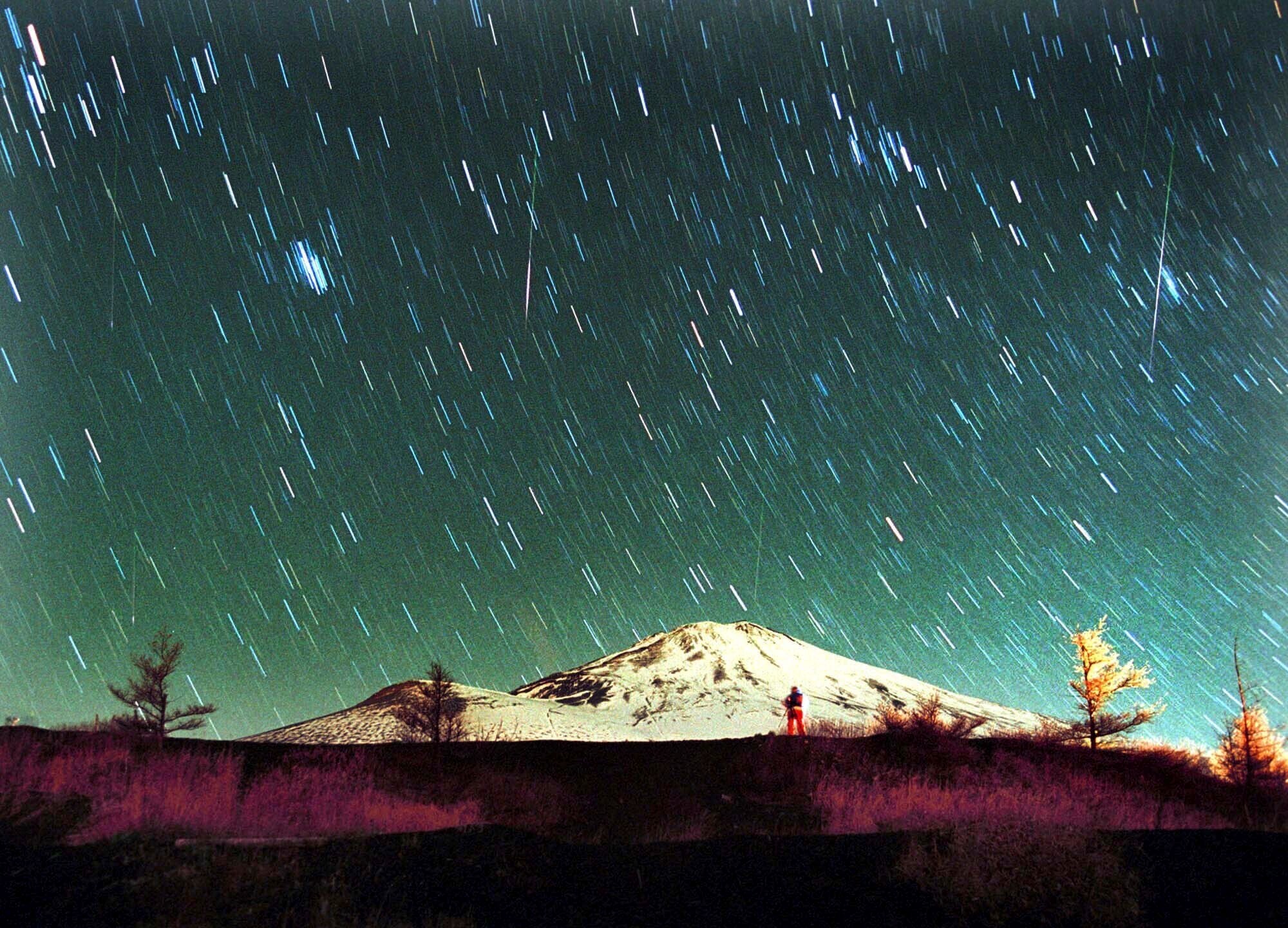 FILE - Leonid meteors are seen streaking across the sky over snow-capped Mount Fuji, Japan's highest mountain, in this 7-minute exposure photo taken, Nov. 19, 2001. (AP Photo/Itsuo Inouye, File)