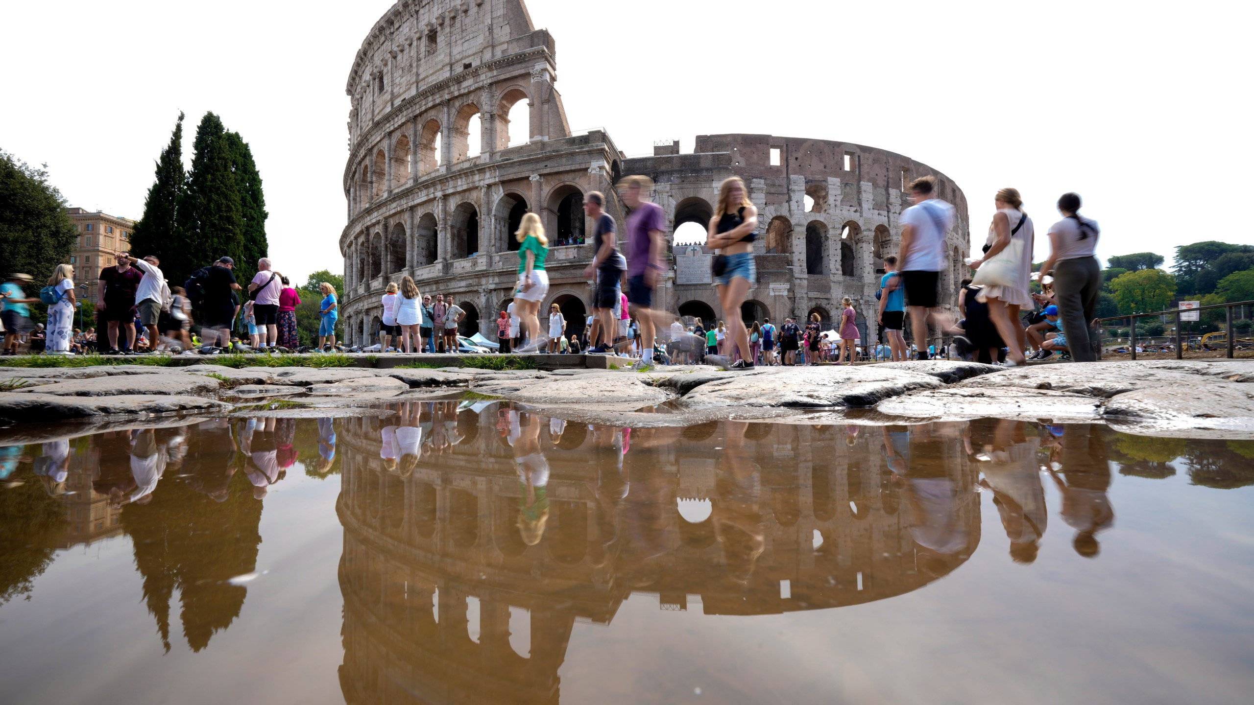 FILE - Tourists walk by the ancient Roman Colosseum as it's reflected in a puddle, in Rome, Sept. 5, 2024. (AP Photo/Andrew Medichini, file)