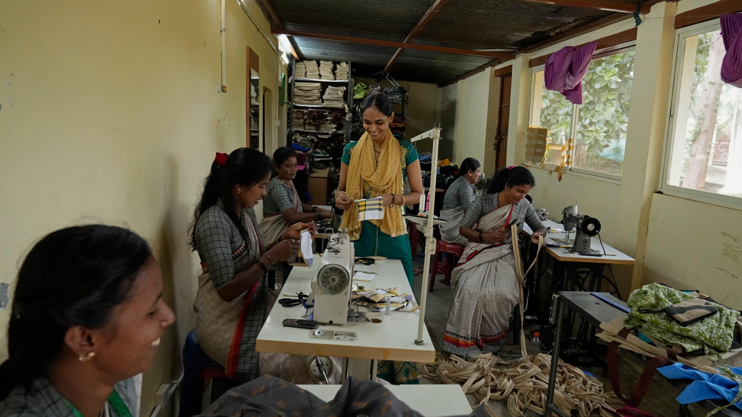 A group of tailors work in a small garage using electric sewing machines to stitch office uniforms and bags at the campus of the Swami Vivekananda Youth Movement, a nongovernmental organization that works to help poor and Indigenous communities, in Kenchanahalli, India, Monday, Sept. 23, 2024. (AP Photo/Aijaz Rahi)