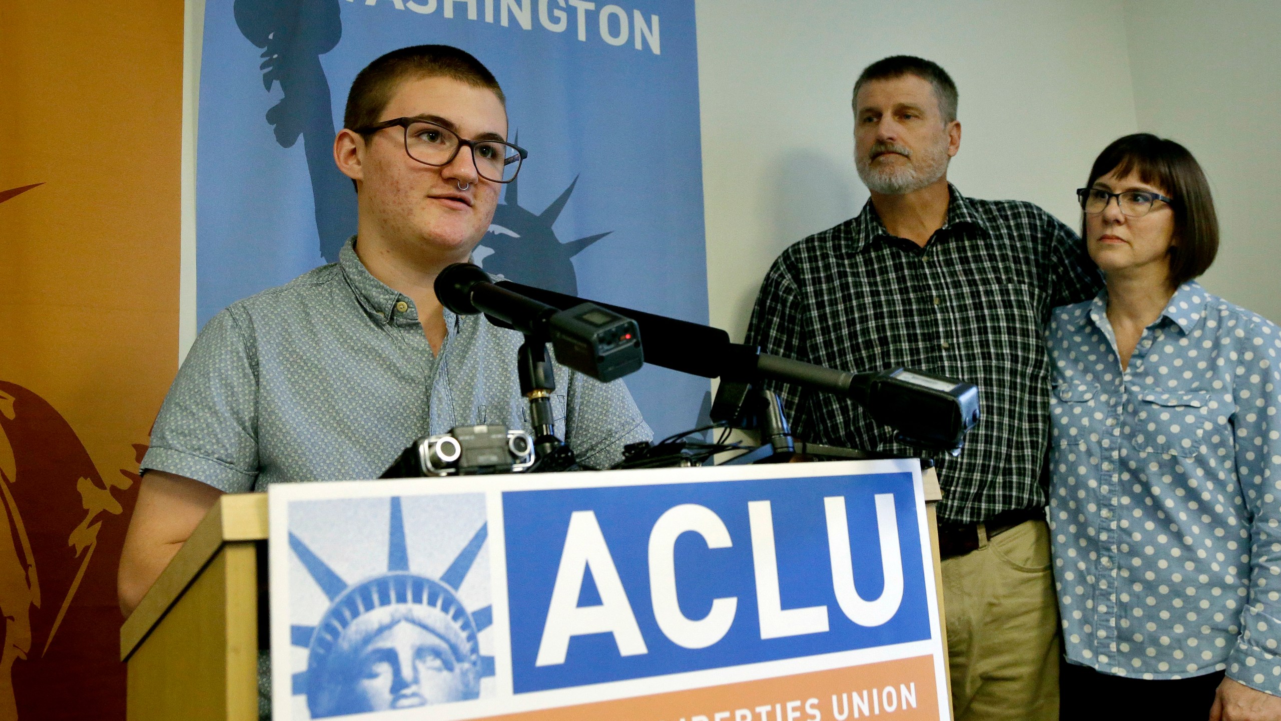 FILE - Paxton Enstad, left, speaks during a news conference about a lawsuit filed over refusal by an insurance plan to cover his gender-reassignment surgery, accompanied by his parents, Cheryl and Mark Enstad, Thursday, Oct. 5, 2017, in Seattle. (AP Photo/Elaine Thompson, File)