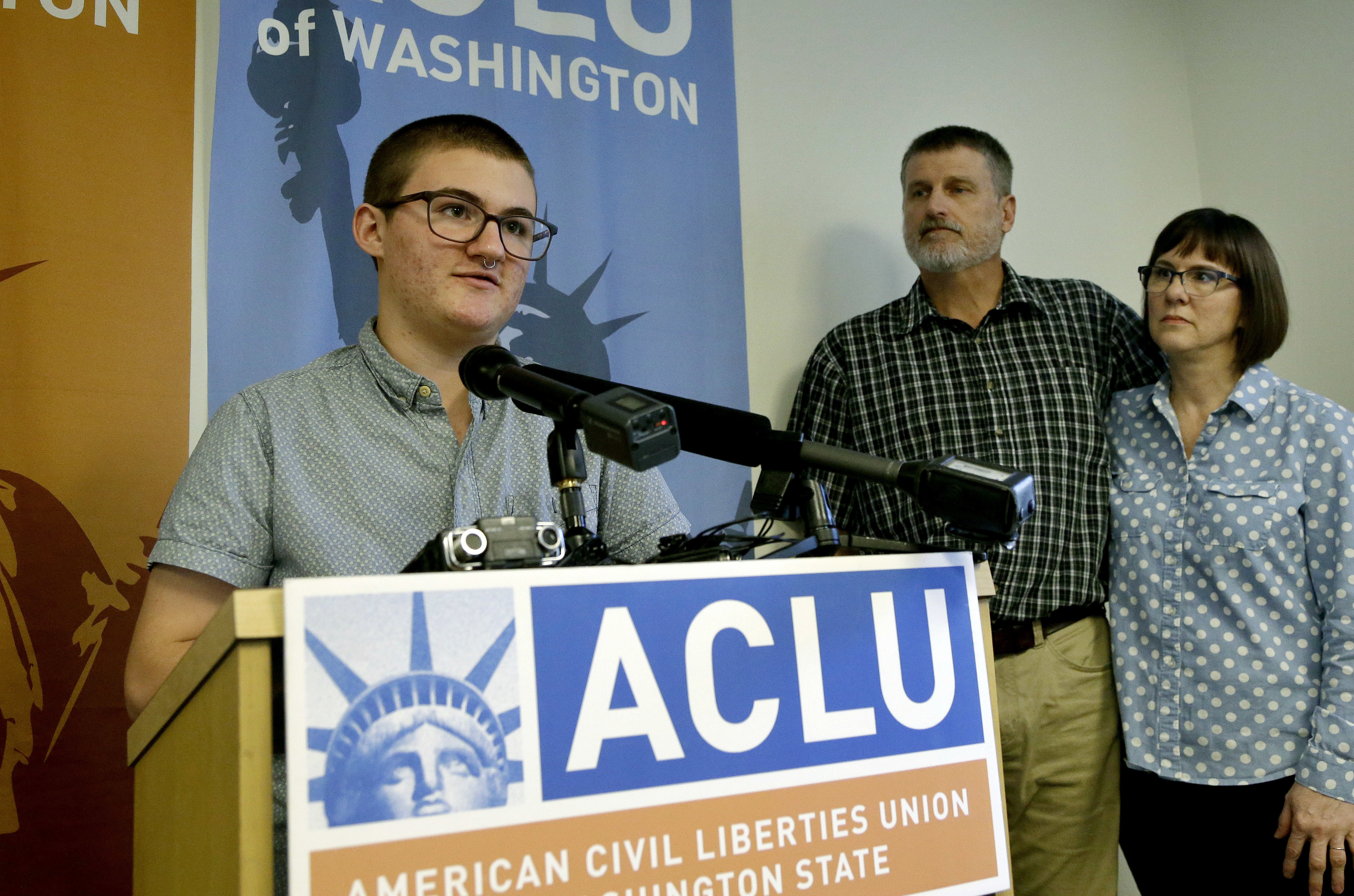 FILE - Paxton Enstad, left, speaks during a news conference about a lawsuit filed over refusal by an insurance plan to cover his gender-reassignment surgery, accompanied by his parents, Cheryl and Mark Enstad, Thursday, Oct. 5, 2017, in Seattle. (AP Photo/Elaine Thompson, File)