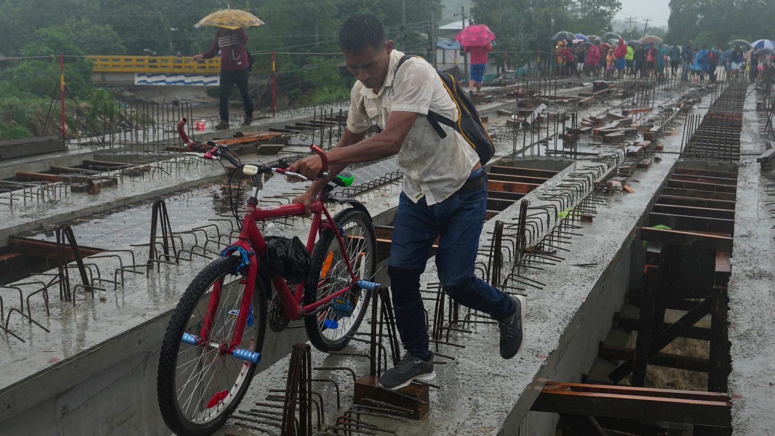 Residents cross a bridge under construction amid rain showers brought on by Tropical Storm Sara, on the outskirts of San Pedro Sula, Honduras, Saturday, Nov. 16, 2024. (AP Photo/Moises Castillo)