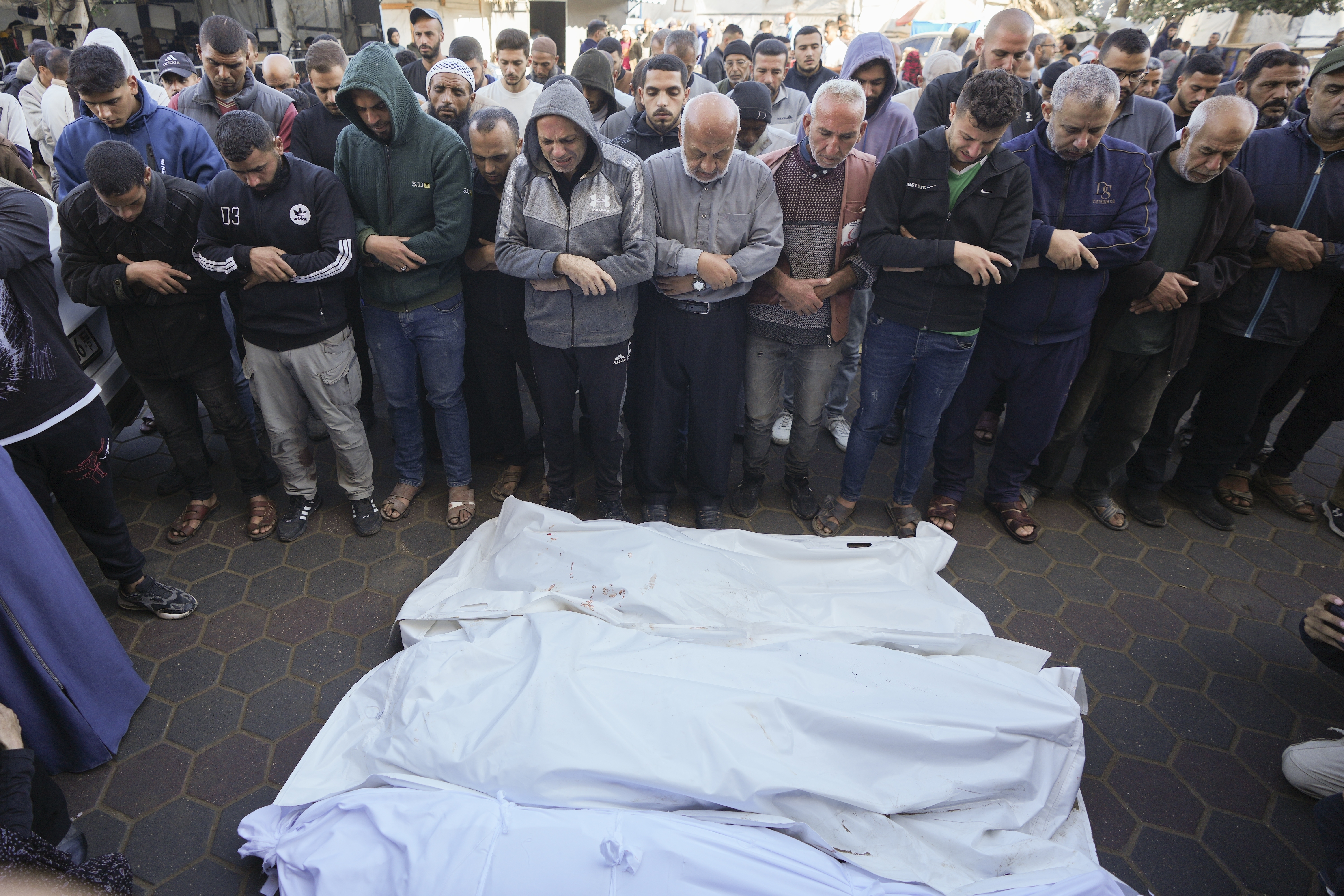 Men pray over the bodies of victims from an Israeli airstrike outside a hospital in Deir al-Balah, Gaza, Sunday Nov. 17, 2024. Palestinian medical officials reported Sunday that Israeli strikes overnight killed 12 people in Central Gaza. One child and five women were counted among them.(AP Photo/Abdel Kareem Hana)