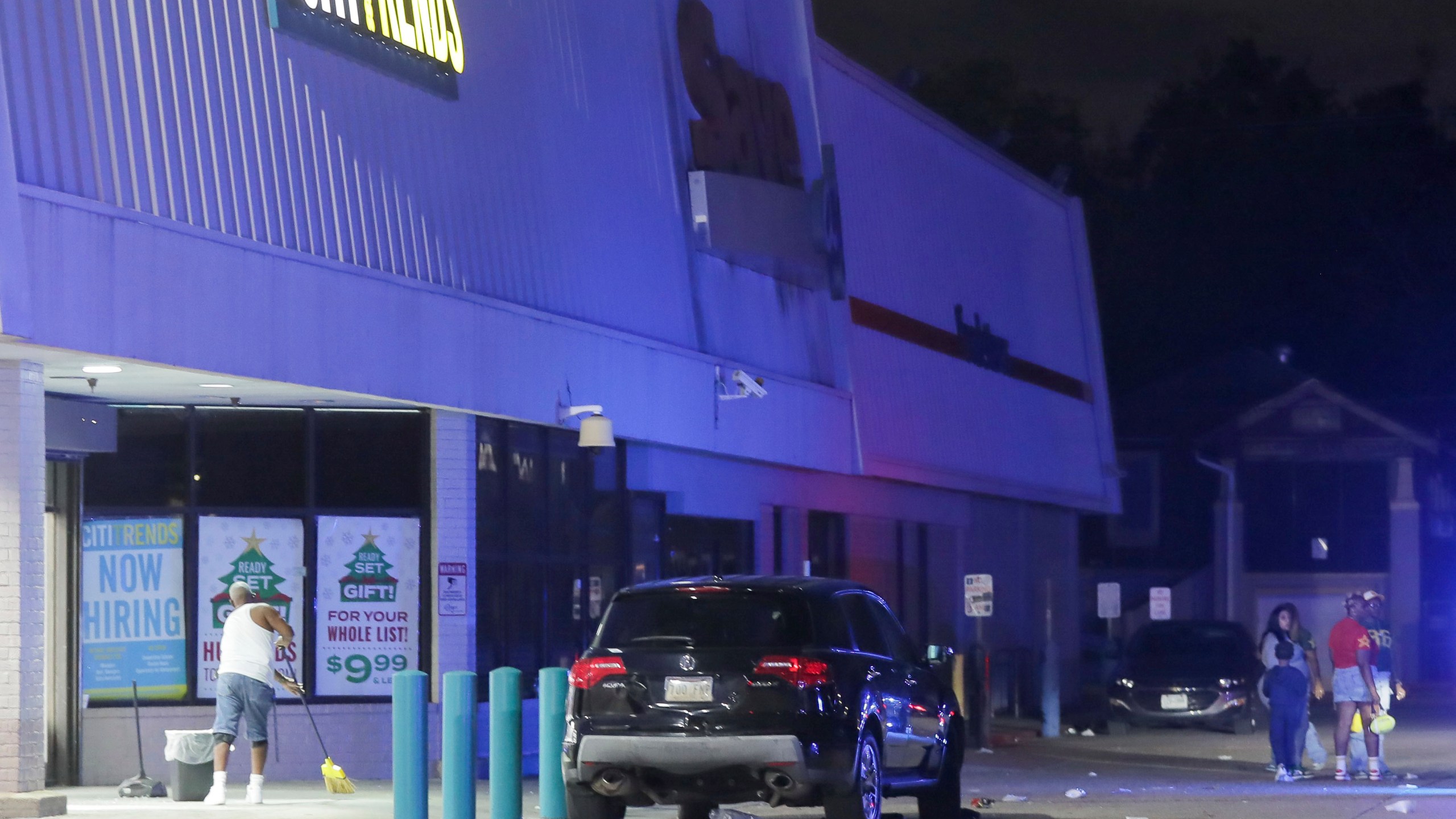 An employee with Cititrends sweeps the ground at a Save O Lot parking lot where several people were shot and killed in New Orleans, Sunday Nov. 17, 2024. (David Grunfeld/The Times-Picayune/The New Orleans Advocate via AP)