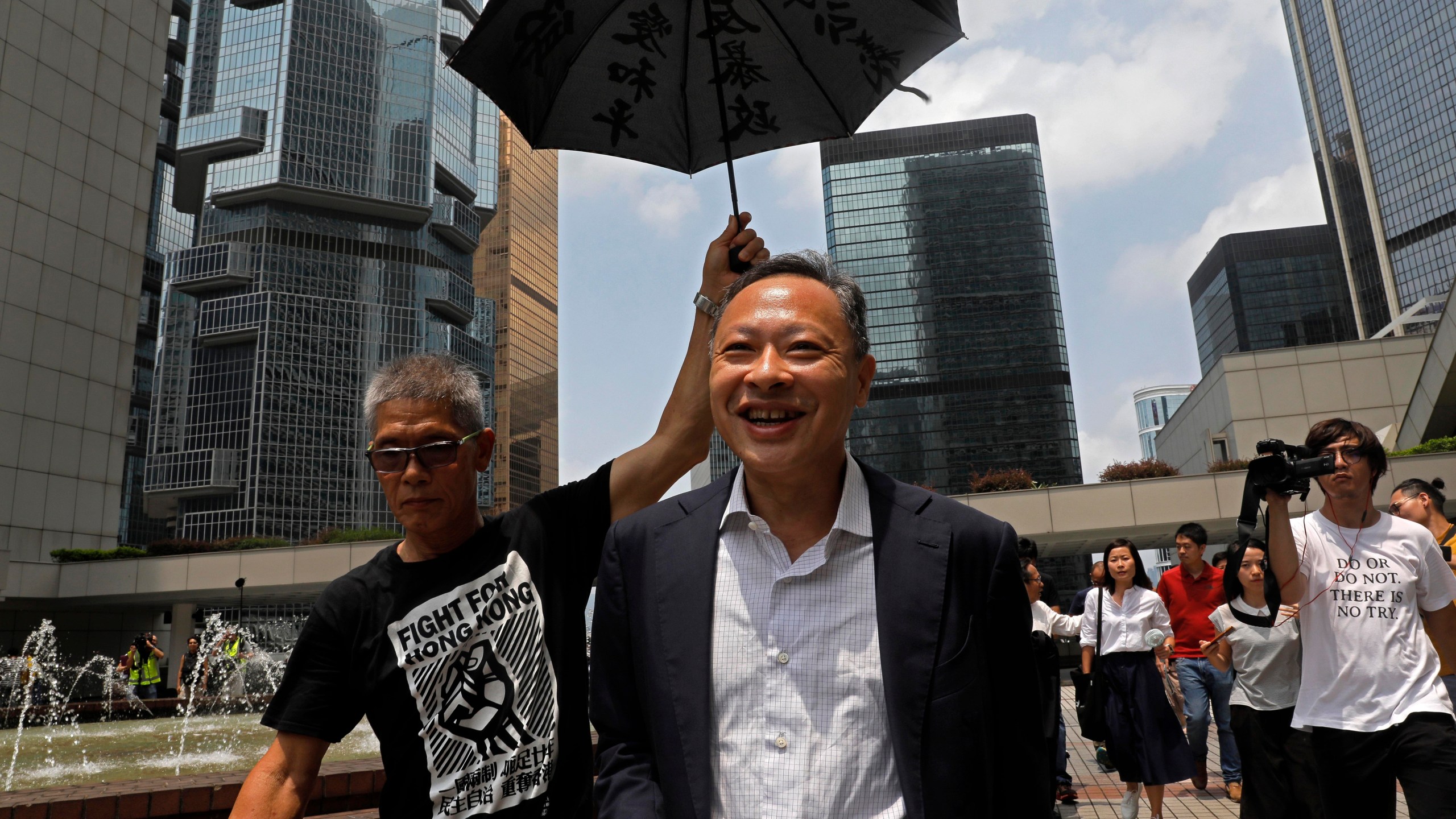 FILE - Occupy Central leader Benny Tai, center, is accompanied by a supporter who raises an umbrella as he leaves high court in Hong Kong, on Aug. 15, 2019. (AP Photo/Vincent Yu, File)