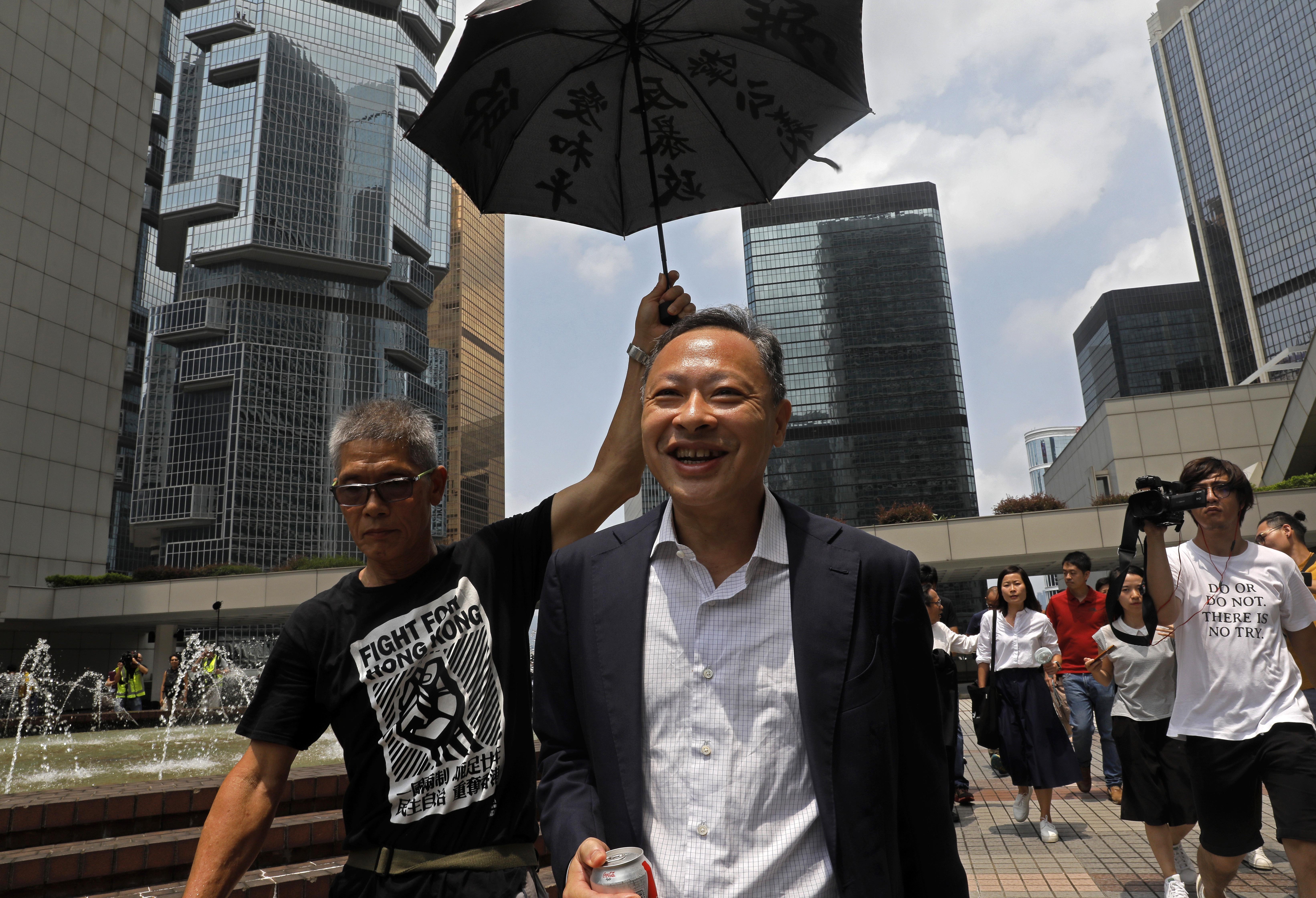 FILE - Occupy Central leader Benny Tai, center, is accompanied by a supporter who raises an umbrella as he leaves high court in Hong Kong, on Aug. 15, 2019. (AP Photo/Vincent Yu, File)