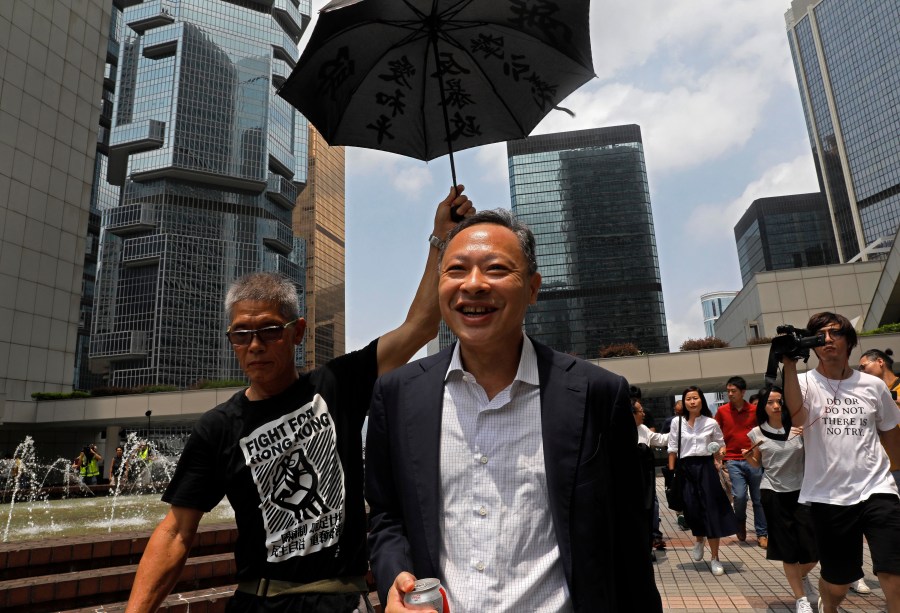 FILE - Occupy Central leader Benny Tai, center, is accompanied by a supporter who raises an umbrella as he leaves high court in Hong Kong, on Aug. 15, 2019. (AP Photo/Vincent Yu, File)