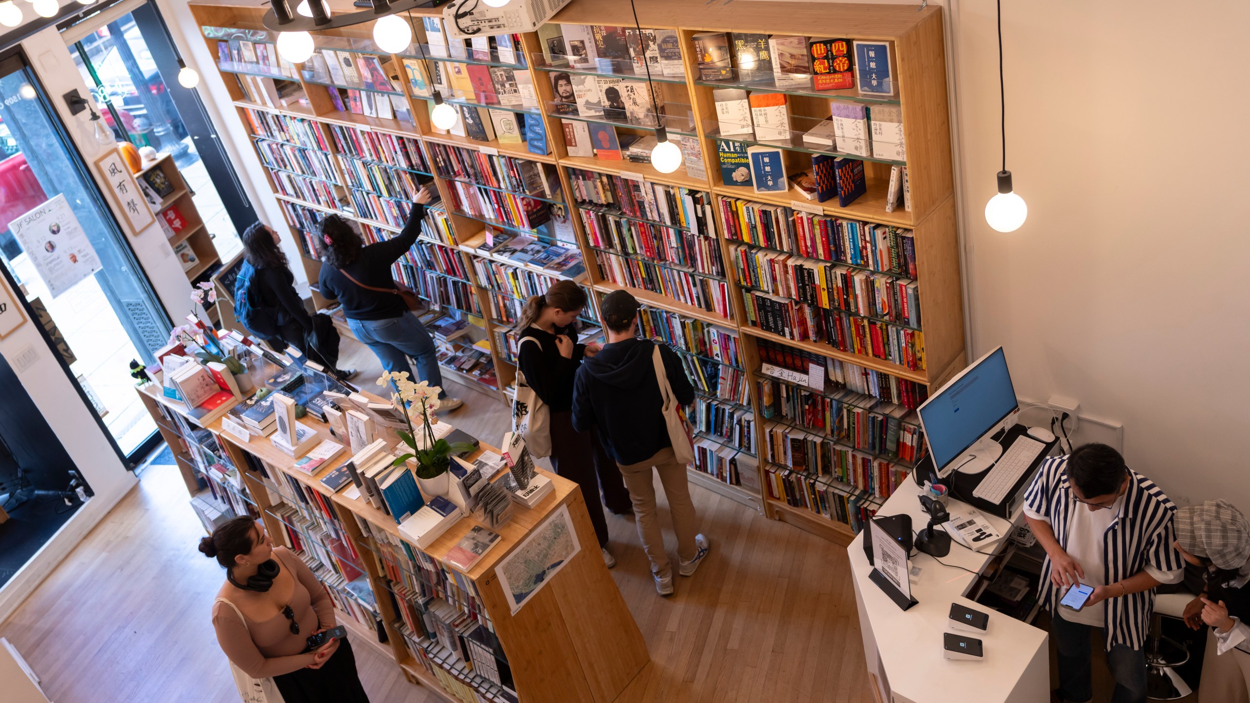 Yu Miao, right, owner of JF Books, looks at his phone as customers browse the books in his bookstore in Washington, Thursday, Oct. 3, 2024. (AP Photo/Ben Curtis)