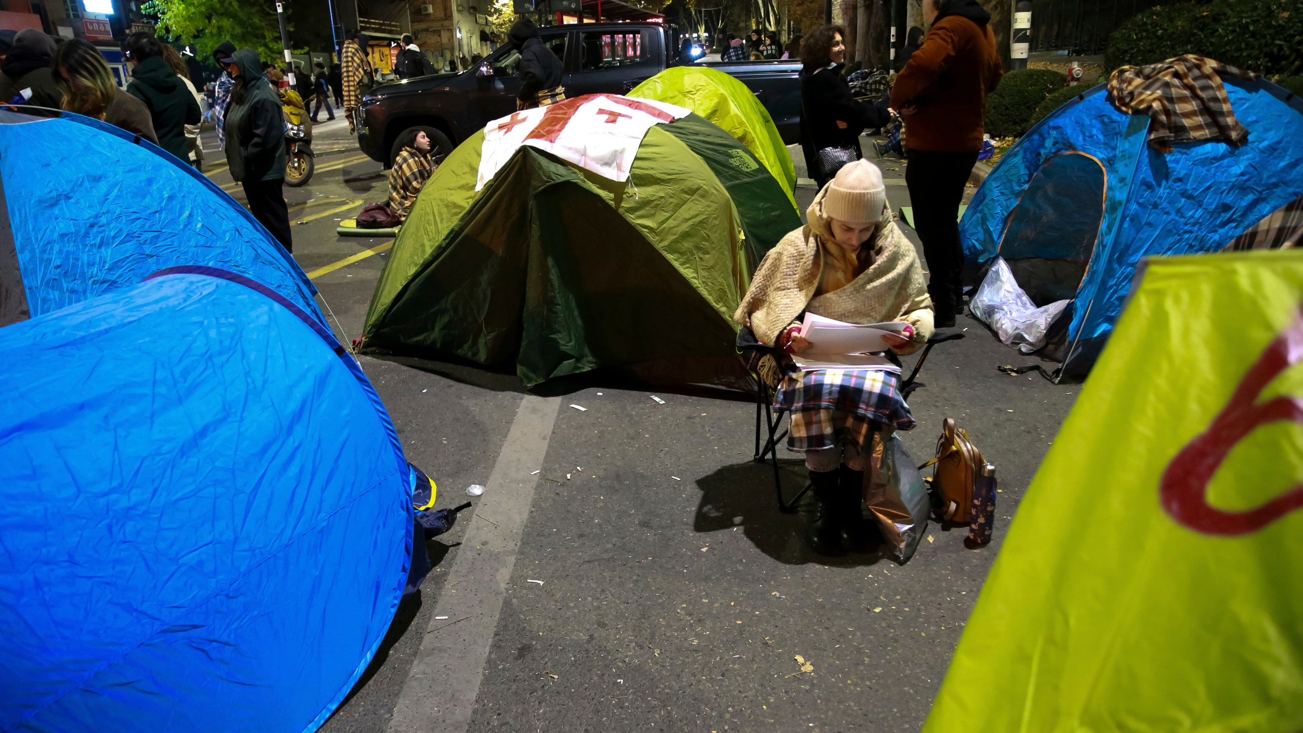 A protester sits between tents during a rally against the results of the parliamentary elections amid allegations that the vote was rigged in Tbilisi, Georgia, early Monday, Nov. 18, 2024. (AP Photo/Zurab Tsertsvadze)