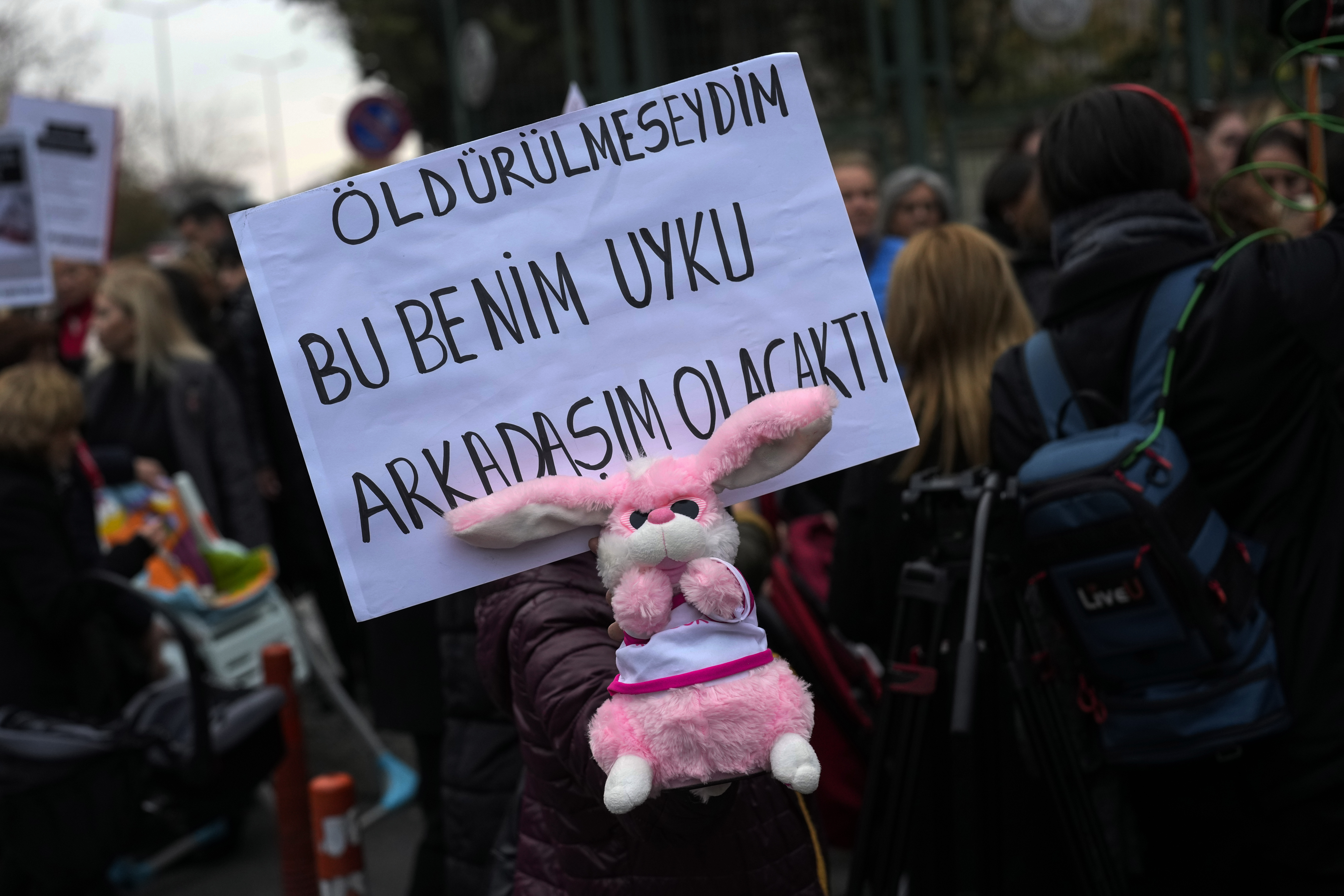 An activist holds a baby toy and a banner with Turkish writing that reads, "If I had not been killed this would have been my sleeping friend" during a protest outside the courthouse where dozens of Turkish healthcare workers including doctors and nurses go on trial for fraud and causing the deaths of 10 infants, in Istanbul, Turkey, Monday Nov, 18, 2024.(AP Photo/Khalil Hamra)