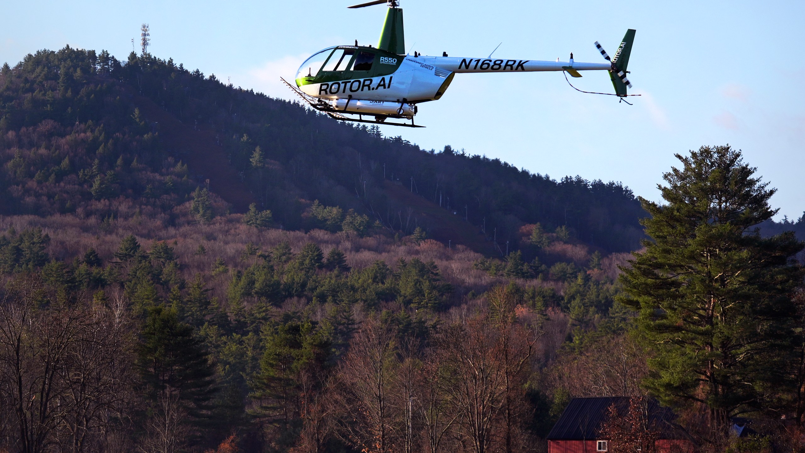 A Rotor Technologies unmanned semi-autonomous helicopter flies near Pat's Peak ski area, rear, during a test flight over Intervale Airport, Monday, Nov. 11, 2024, in Henniker, N.H. (AP Photo/Charles Krupa)