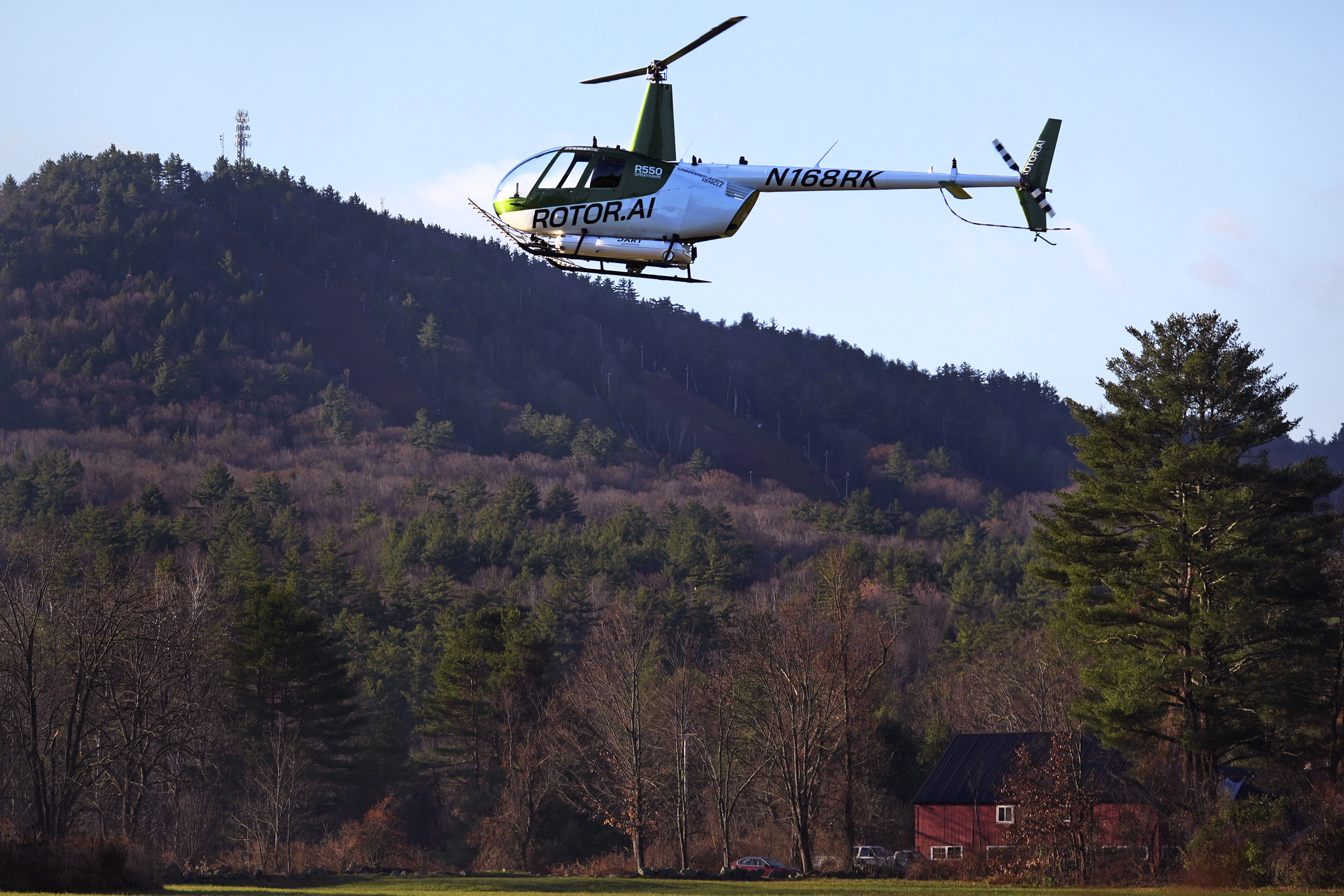 A Rotor Technologies unmanned semi-autonomous helicopter flies near Pat's Peak ski area, rear, during a test flight over Intervale Airport, Monday, Nov. 11, 2024, in Henniker, N.H. (AP Photo/Charles Krupa)