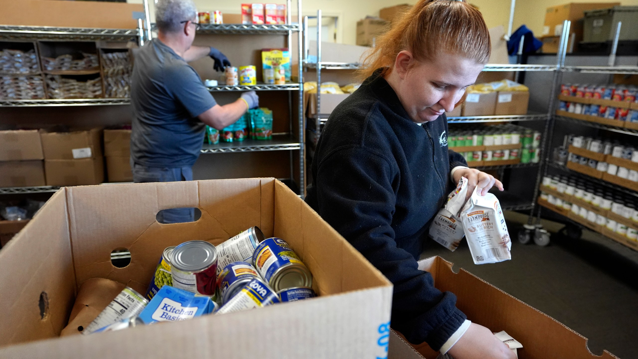 Volunteer Madison Turner, of Providence, R.I. right, organizes food items in a food pantry at Federal Hill House, Tuesday, Nov. 12, 2024, in Providence, R.I. (AP Photo/Steven Senne)