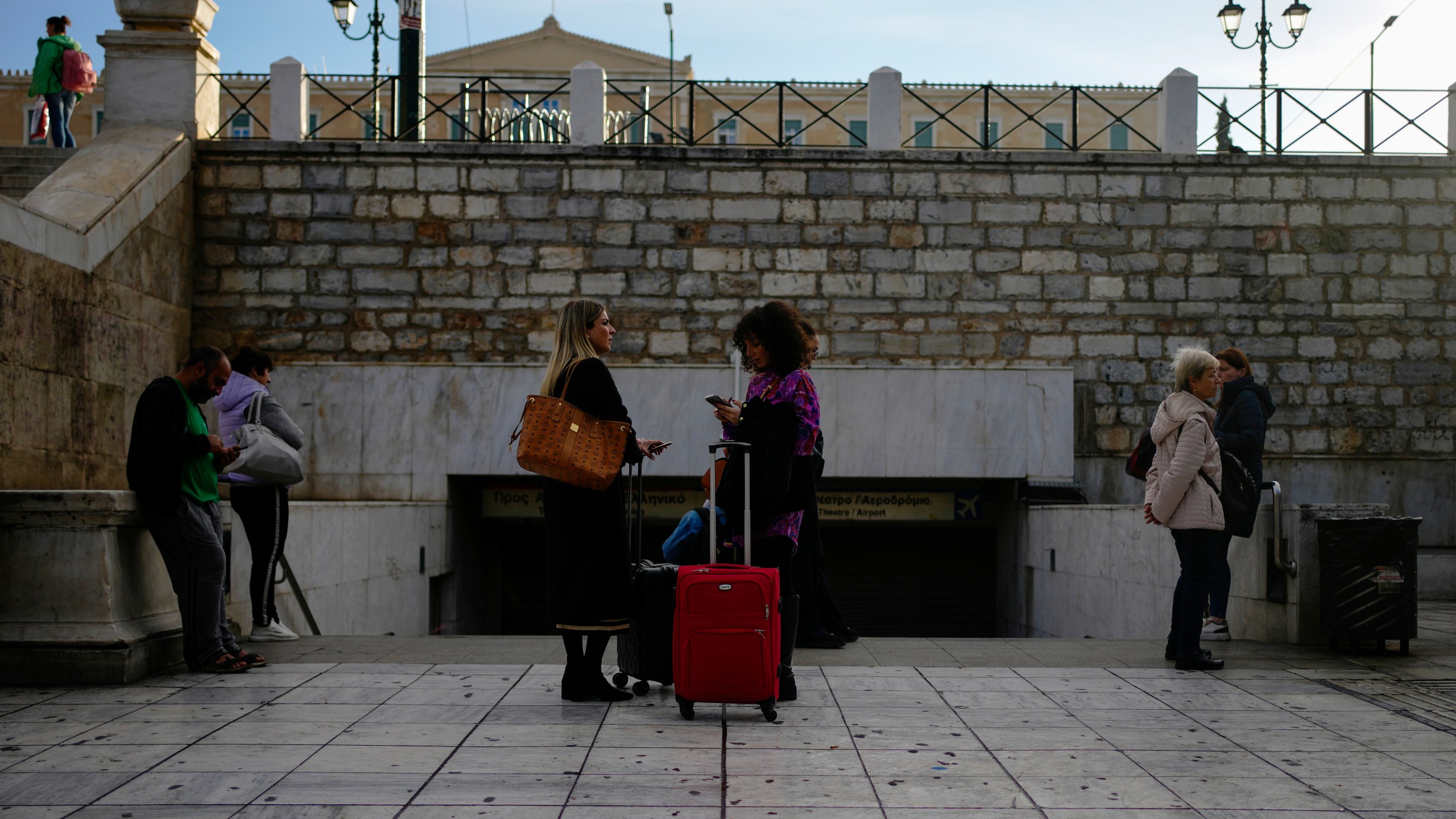 Commuters stand outside the closed main metro Syntagma station, during a nationwide general strike organized by private and public sector unions demanding for better wages, in Athens, Greece, Wednesday, Nov. 20, 2024. (AP Photo/Thanassis Stavrakis)