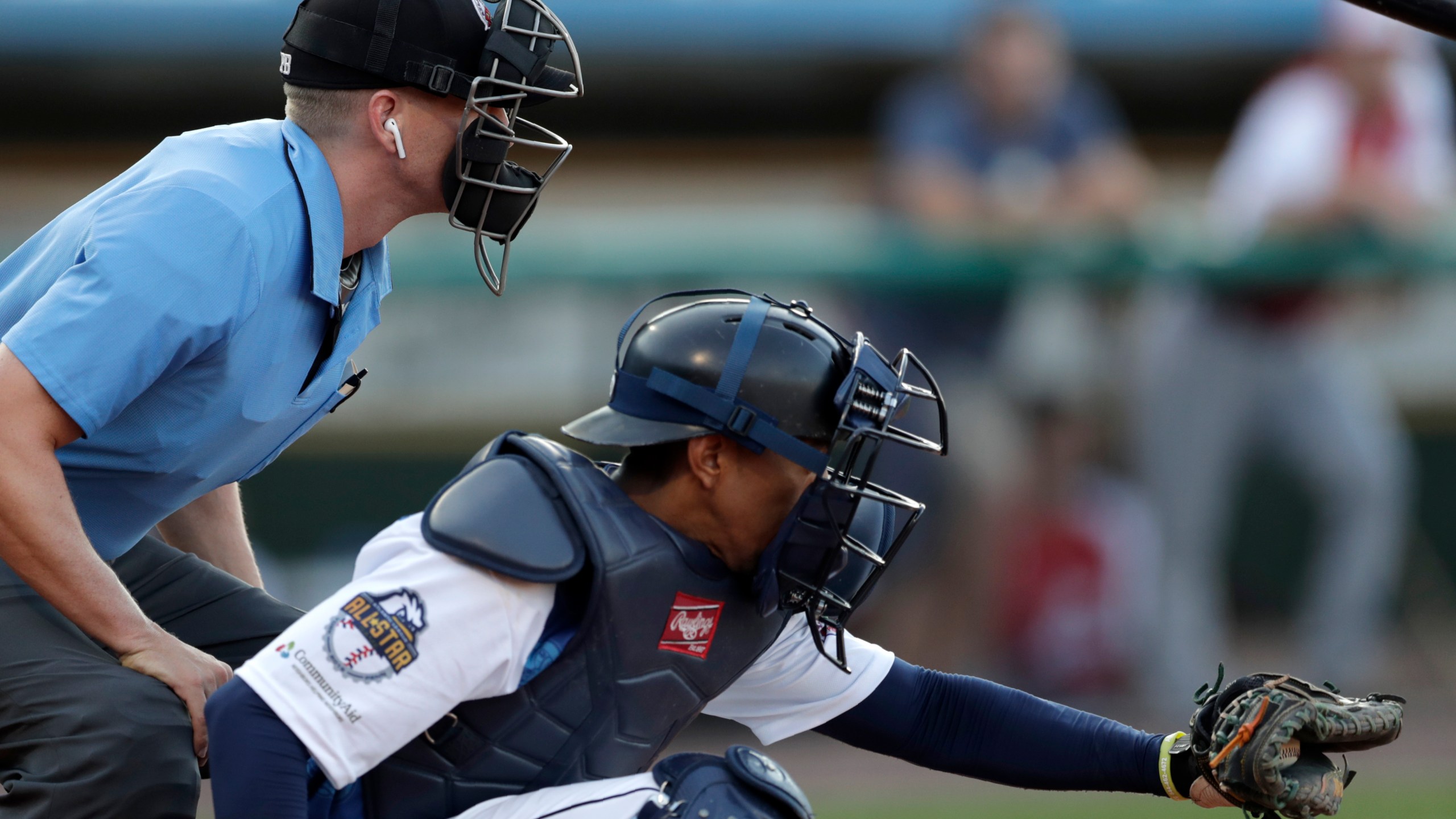 FILE -Home plate umpire Brian deBrauwere, left, huddles behind Freedom Division catcher James Skelton, of the York Revolution, as the official wears an earpiece during the first inning of the Atlantic League All-Star minor league baseball game, Wednesday, July 10, 2019, in York, Pa. Major League Baseball will test robot umpires as part of a challenge system during spring training at 13 ballparks hosting 19 teams, which could lead to regular-season use in 2026. (AP Photo/Julio Cortez, File)