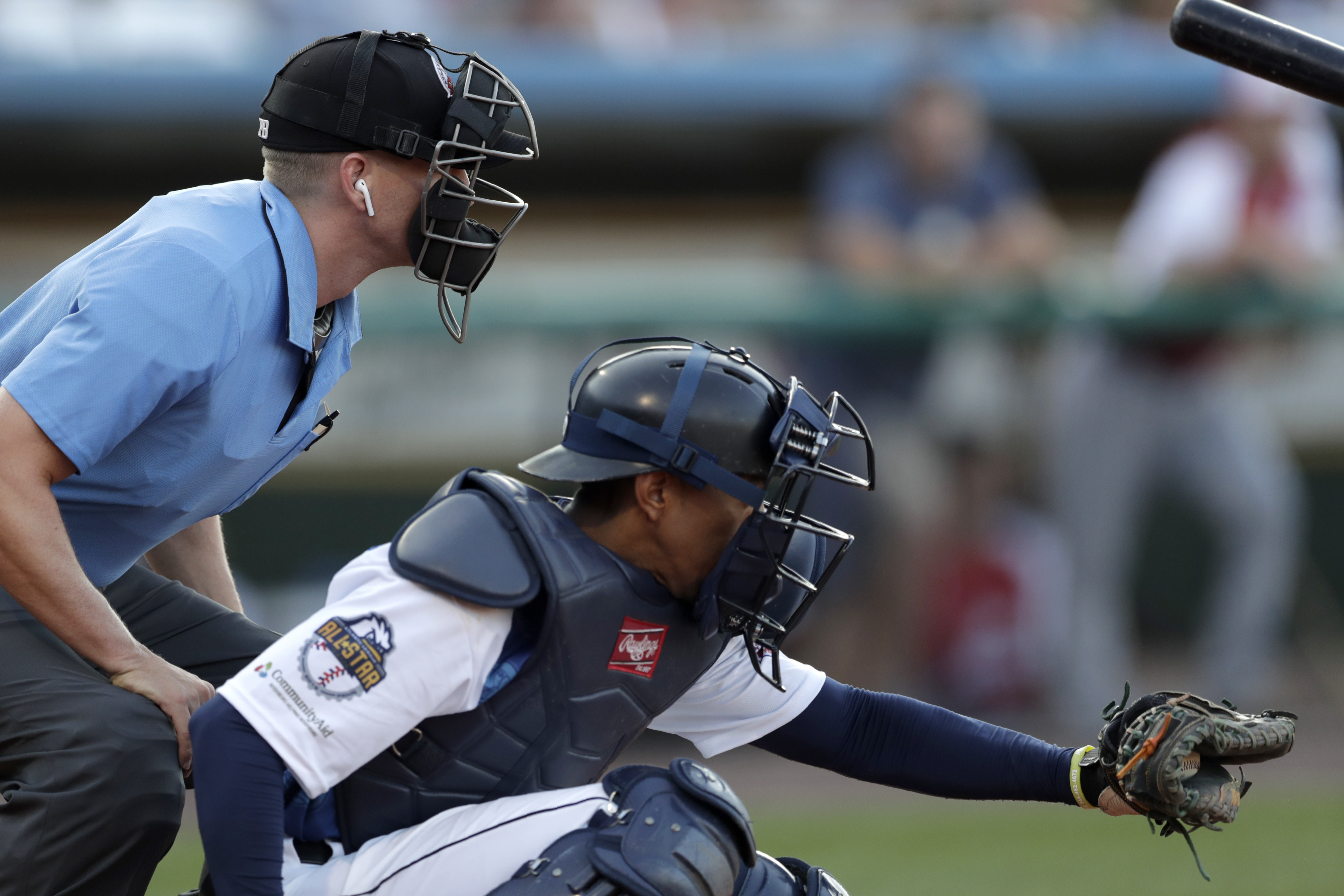 FILE -Home plate umpire Brian deBrauwere, left, huddles behind Freedom Division catcher James Skelton, of the York Revolution, as the official wears an earpiece during the first inning of the Atlantic League All-Star minor league baseball game, Wednesday, July 10, 2019, in York, Pa. Major League Baseball will test robot umpires as part of a challenge system during spring training at 13 ballparks hosting 19 teams, which could lead to regular-season use in 2026. (AP Photo/Julio Cortez, File)