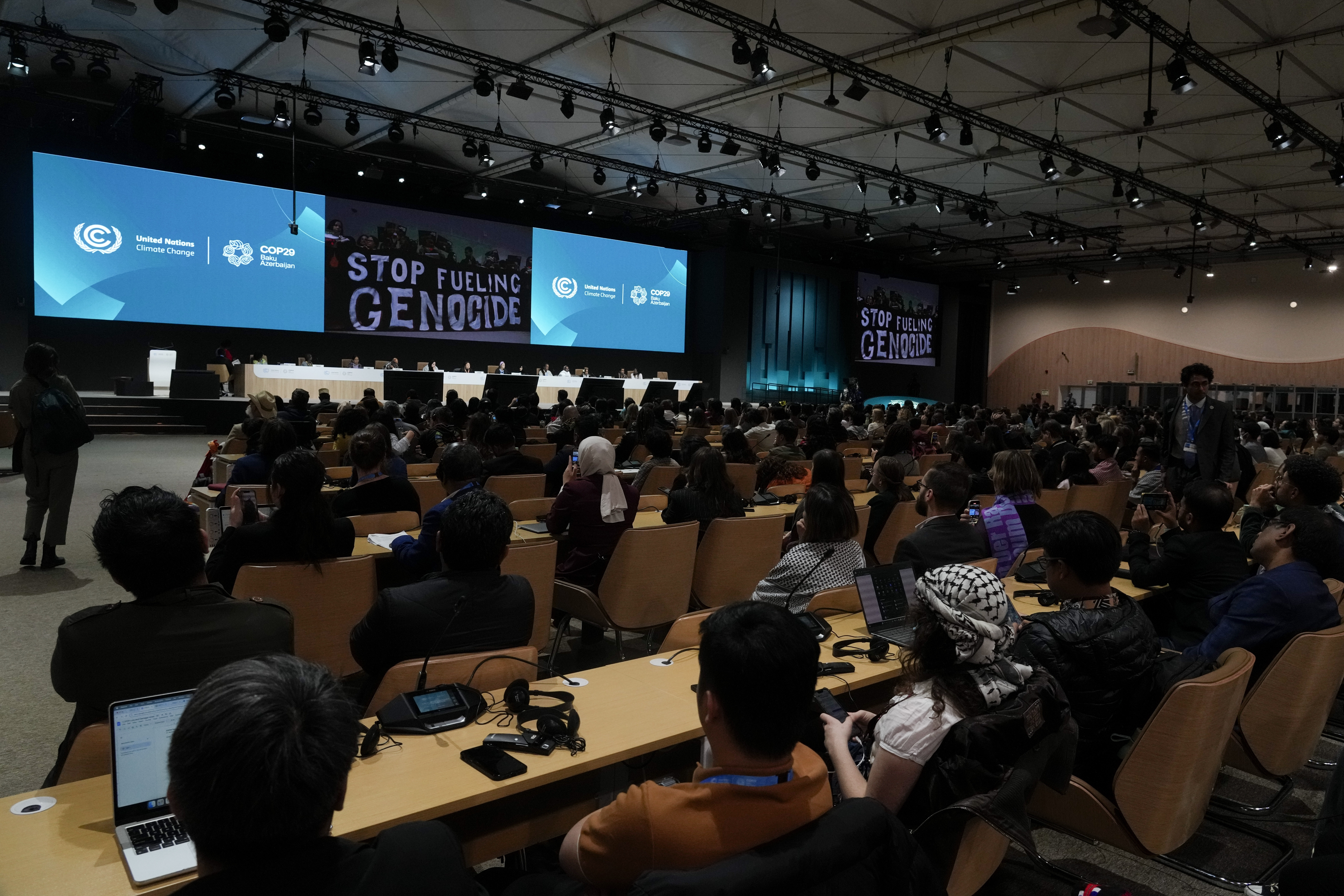 Activists display signs that read "stop fueling genocide" during the People's Plenary at the COP29 U.N. Climate Summit, Thursday, Nov. 21, 2024, in Baku, Azerbaijan. (AP Photo/Rafiq Maqbool)