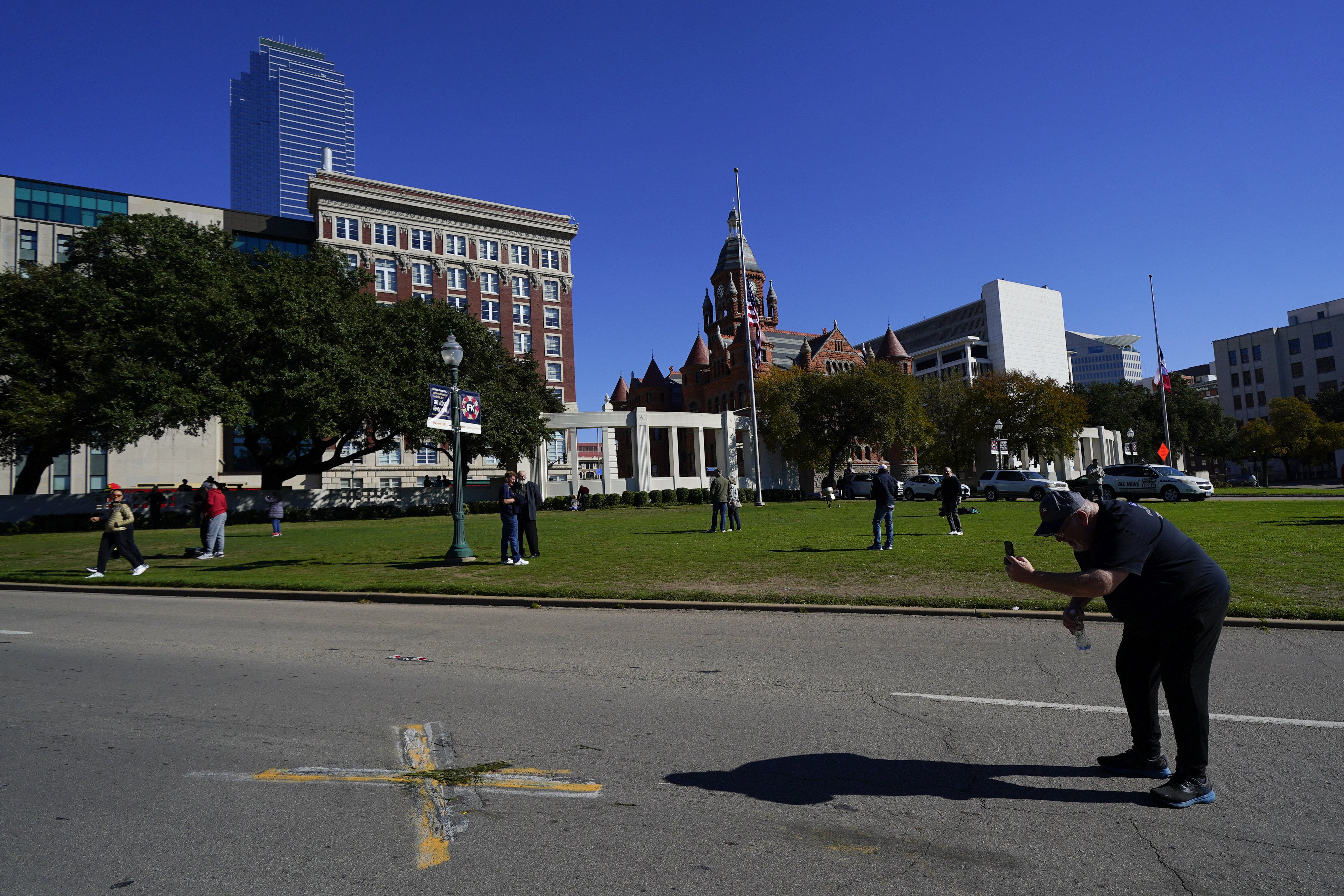 FILE - A person uses a cell phone to capture images of an X on Elm Street at Dealey Plaza, one of two spots marked where President John F. Kennedy was shot, as people gather on the 60th anniversary of his assassination, Nov. 22, 2023, in Dallas. (AP Photo/Julio Cortez, File)