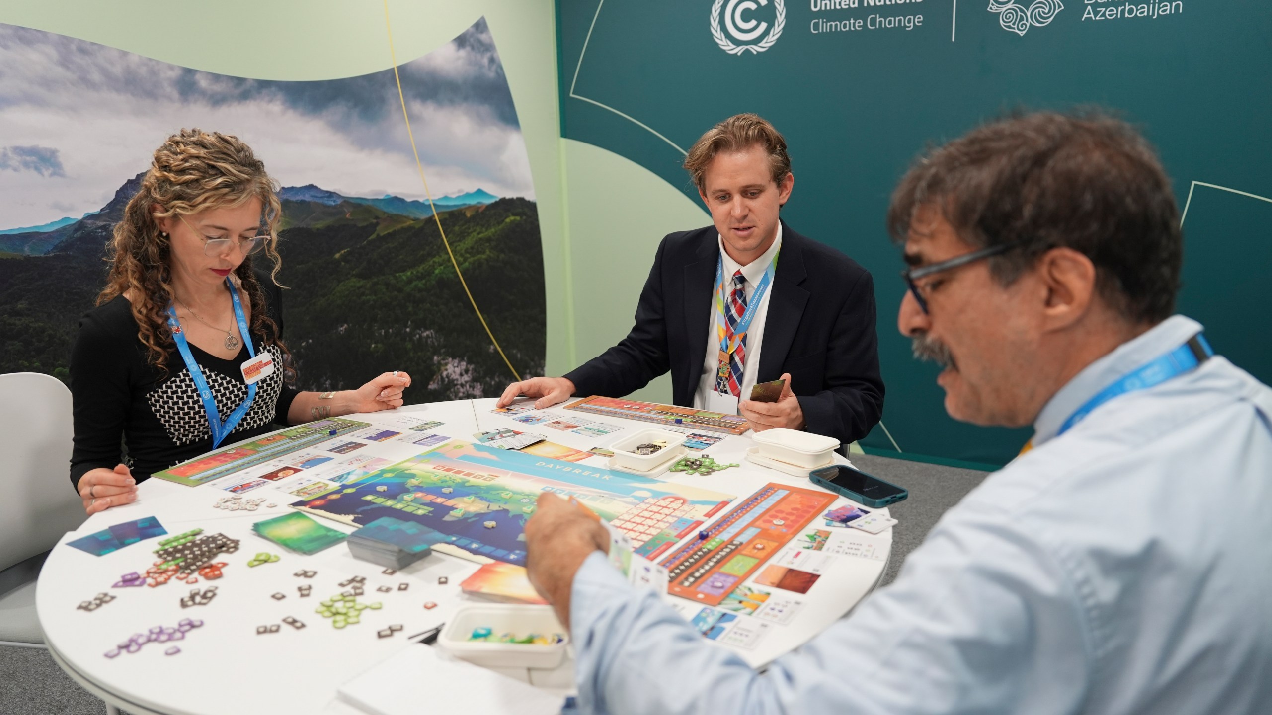 Courtney Howard, of Global Climate and Health Alliance and Nathan Cogswell, of World Resources Institute, center, play Daybreak, a game where players are supposed to work together to find a way to curb climate change, with Seth Borenstein, Associated Press science writer, at the COP29 U.N. Climate Summit, Tuesday, Nov. 19, 2024, in Baku, Azerbaijan. (AP Photo/Joshua A. Bickel)