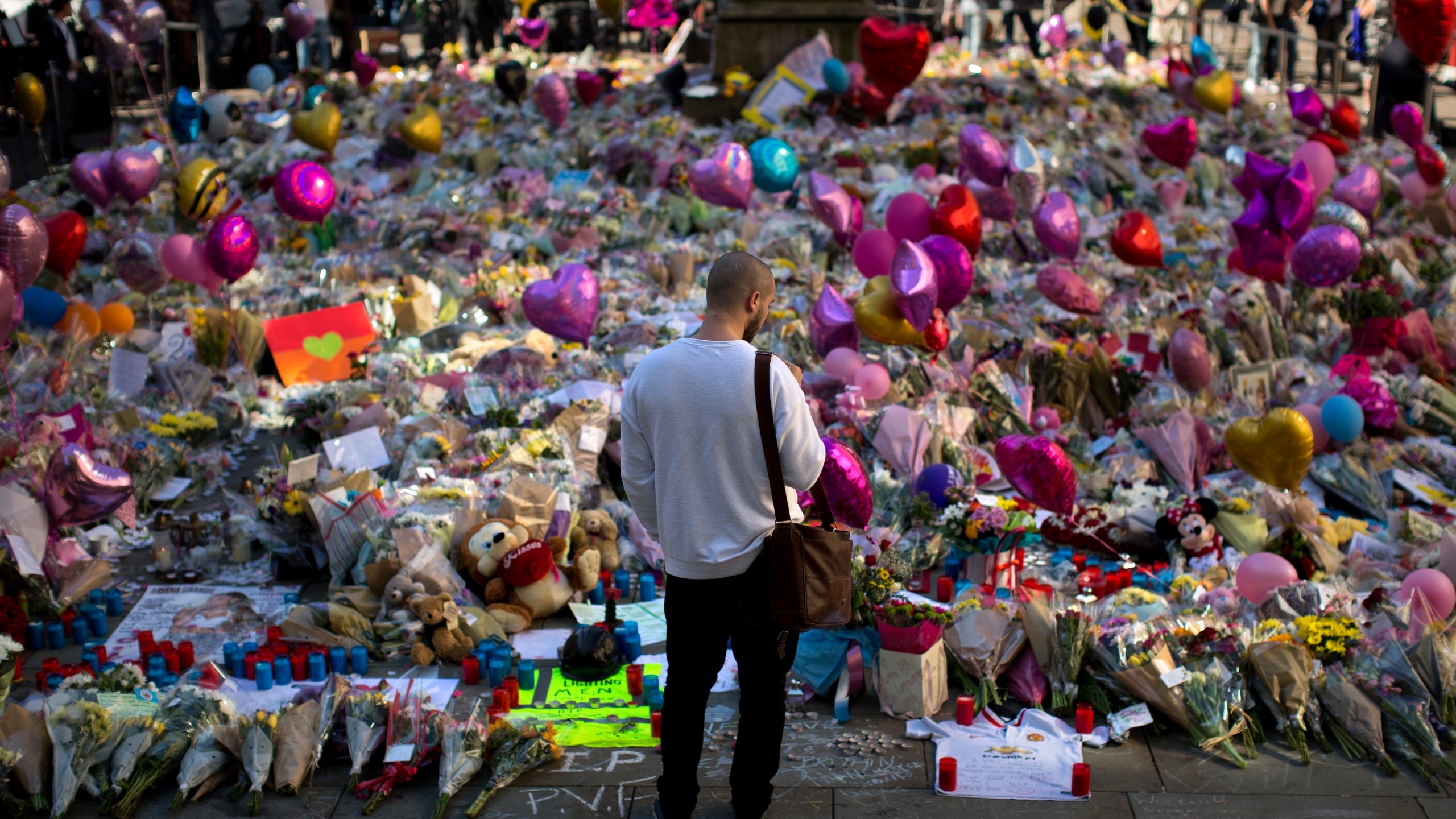 FILE - A man stands next to flowers for the victims of a bombing at St. Ann's Square in central Manchester, England, May 26, 2017. (AP Photo/Emilio Morenatti, File)