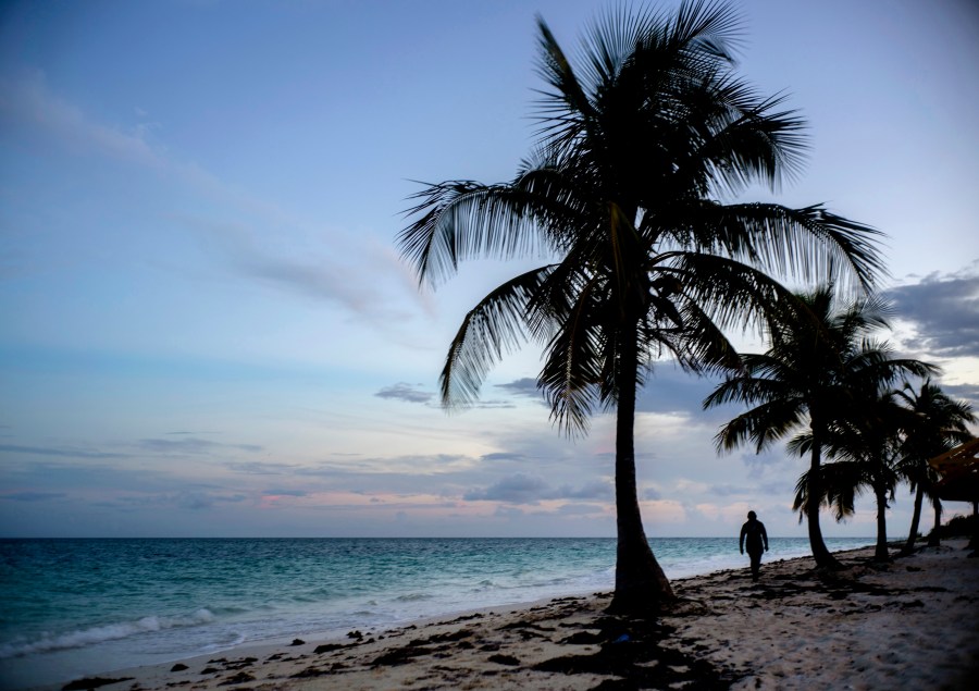 FILE - A woman walks along an ocean coast in Freeport, The Bahamas, Aug. 31, 2019. (AP Photo/Ramon Espinosa, File)