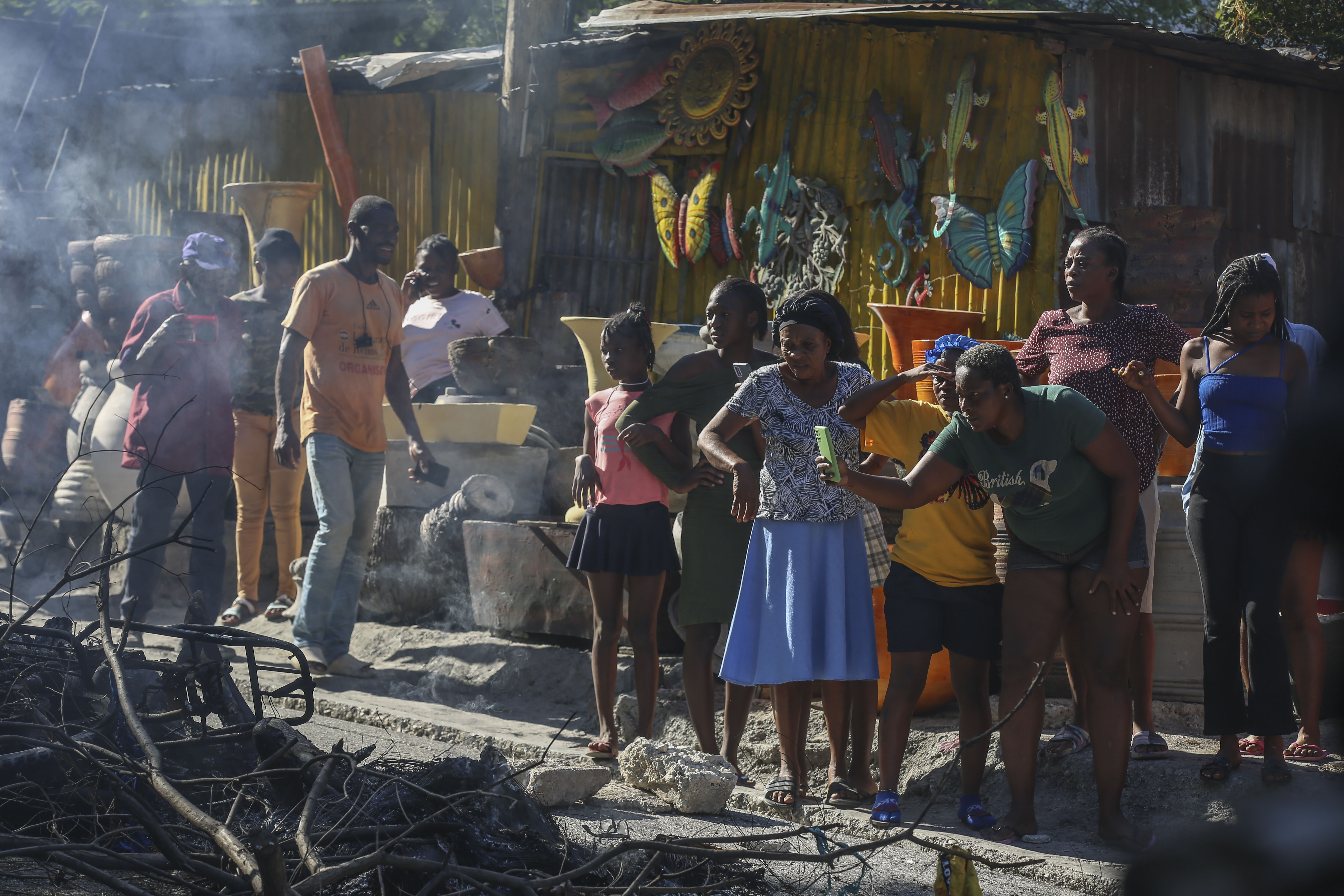 A woman films a scene where the bodies of suspected gang members who were set on fire by residents sit in a heap in the middle of a road, in the Pétion-Ville neighborhood of Port-au-Prince, Haiti, Tuesday, Nov. 19, 2024. (AP Photo/Odelyn Joseph)