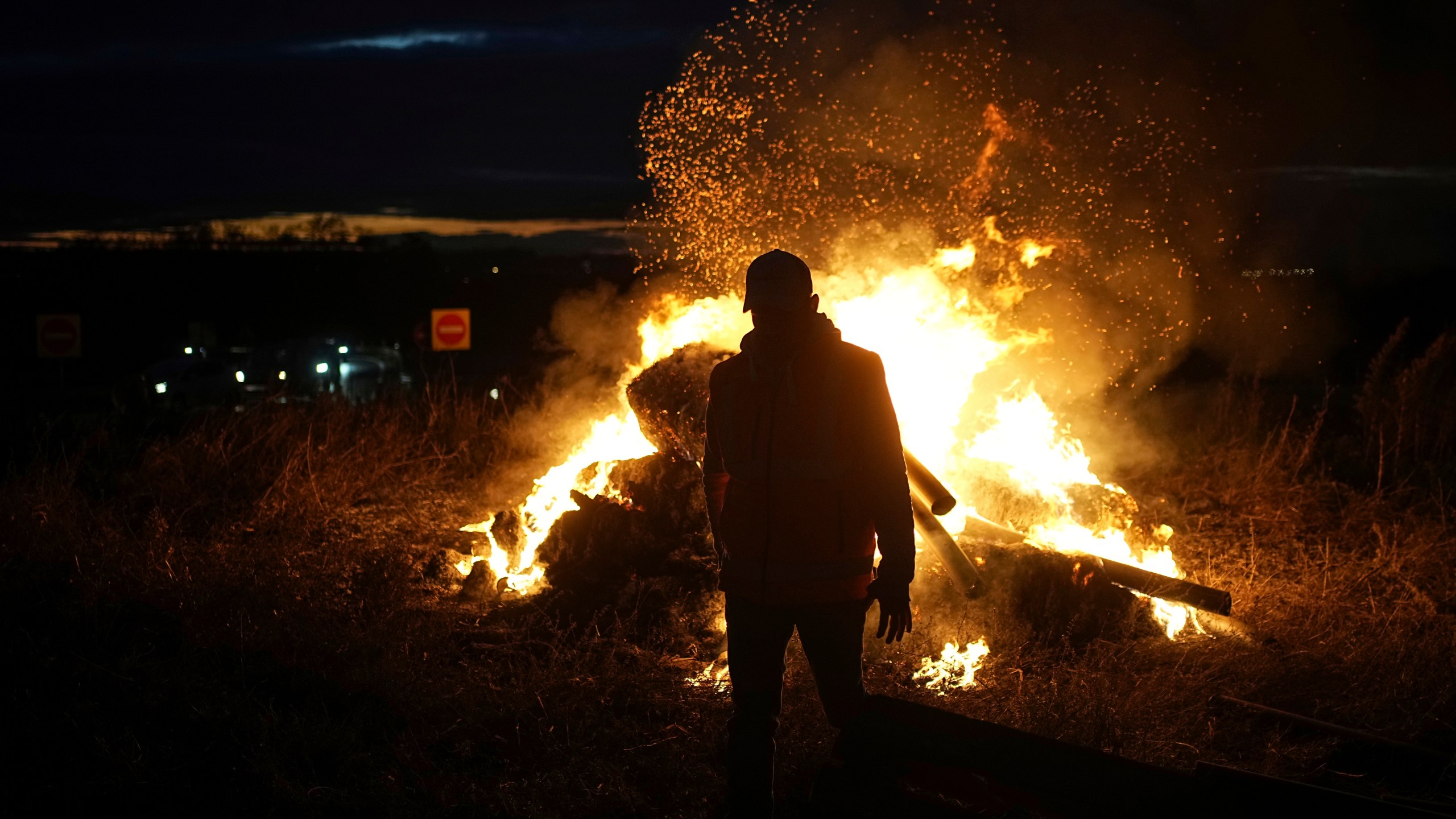 FILE - A farmer walks by a fire as farmers protest against the EU-Mercosur trade agreement, in Saint-Laurent-de-Mure, near Lyon, central France, Monday, Nov. 18, 2024. (AP Photo/Laurent Cipriani, File)