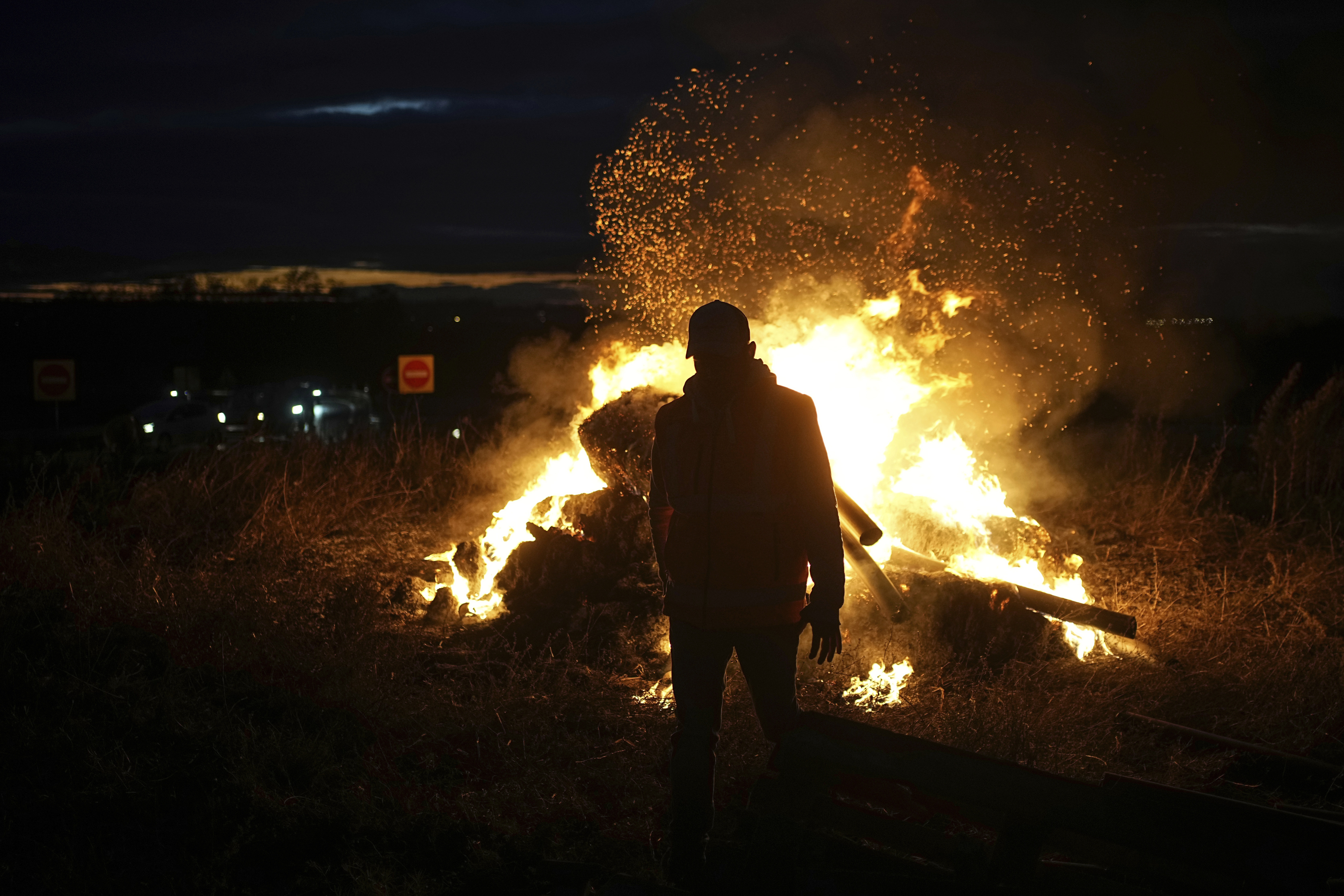 FILE - A farmer walks by a fire as farmers protest against the EU-Mercosur trade agreement, in Saint-Laurent-de-Mure, near Lyon, central France, Monday, Nov. 18, 2024. (AP Photo/Laurent Cipriani, File)