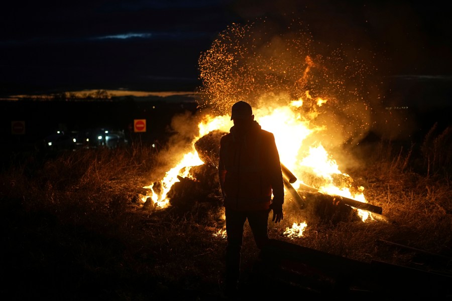 FILE - A farmer walks by a fire as farmers protest against the EU-Mercosur trade agreement, in Saint-Laurent-de-Mure, near Lyon, central France, Monday, Nov. 18, 2024. (AP Photo/Laurent Cipriani, File)