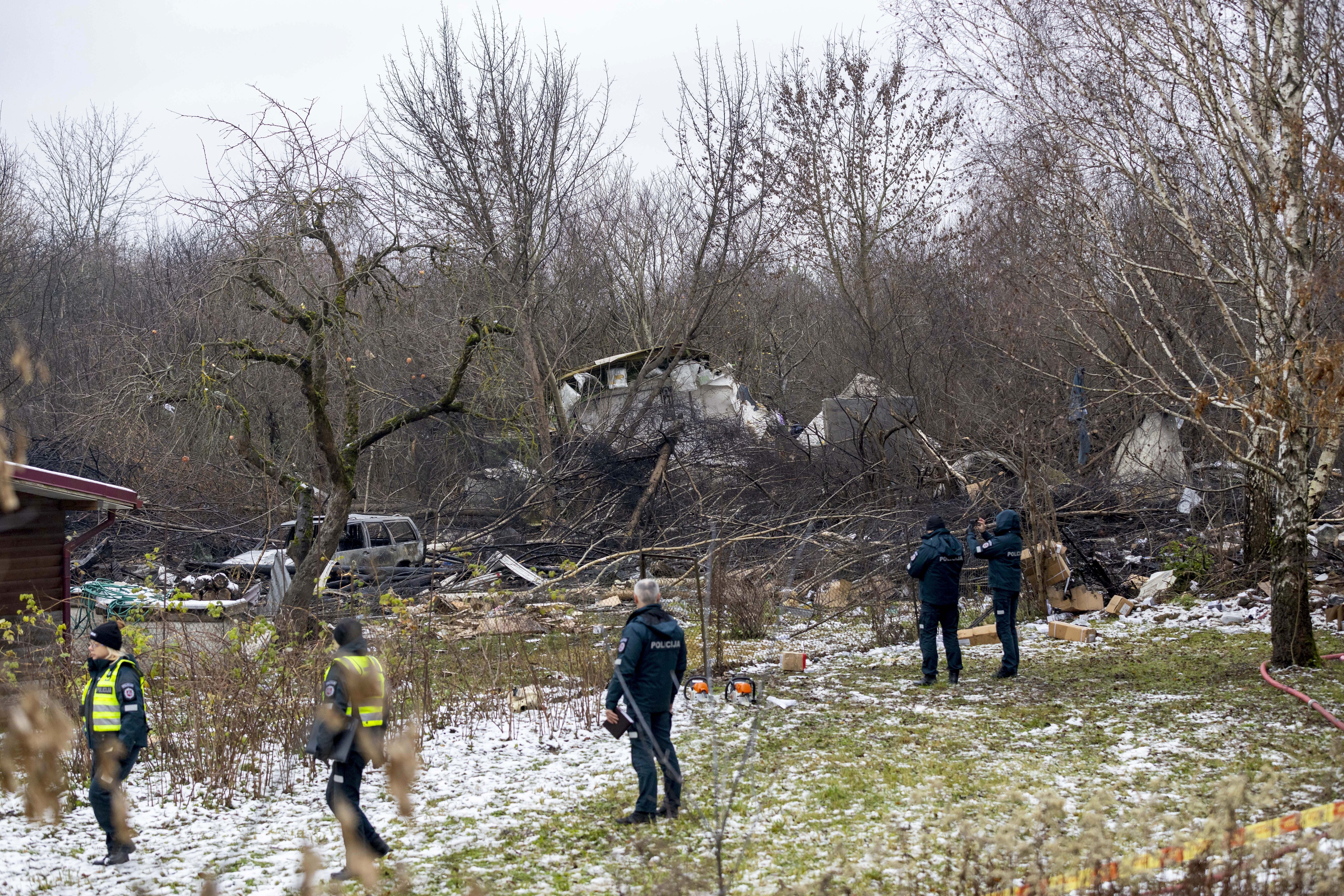 Lithuanian Emergency Ministry employees and police officers stand near the place where a DHL cargo plane crashed into a house near Vilnius, Lithuania, Monday, Nov. 25, 2024. (AP Photo/Mindaugas Kulbis)