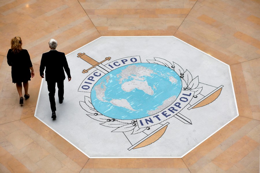 FILE - People walk on the Interpol logo at the international police agency headquarters in Lyon, France, on Nov. 8, 2018. (AP Photo/Laurent Cipriani, File)