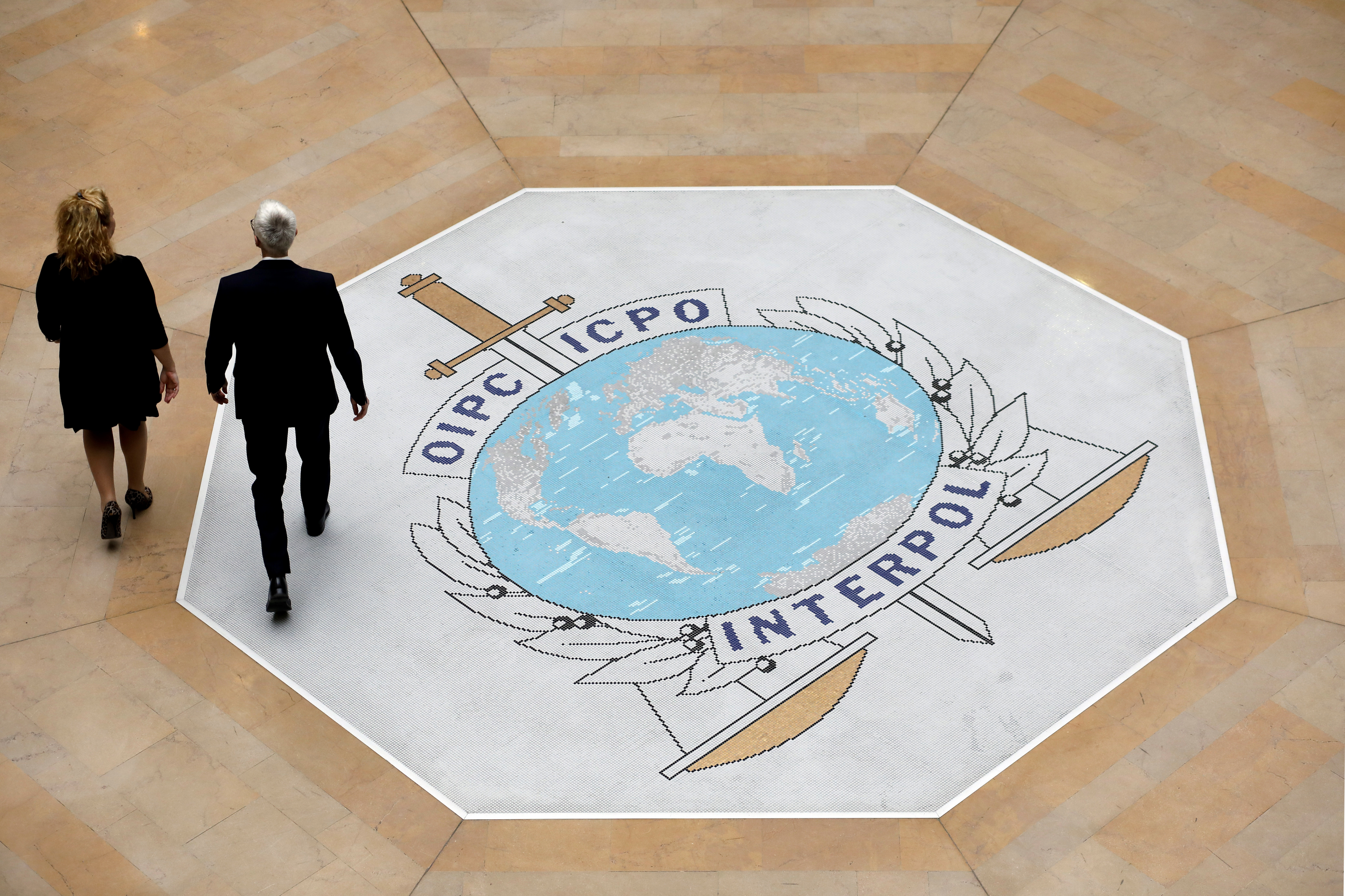 FILE - People walk on the Interpol logo at the international police agency headquarters in Lyon, France, on Nov. 8, 2018. (AP Photo/Laurent Cipriani, File)