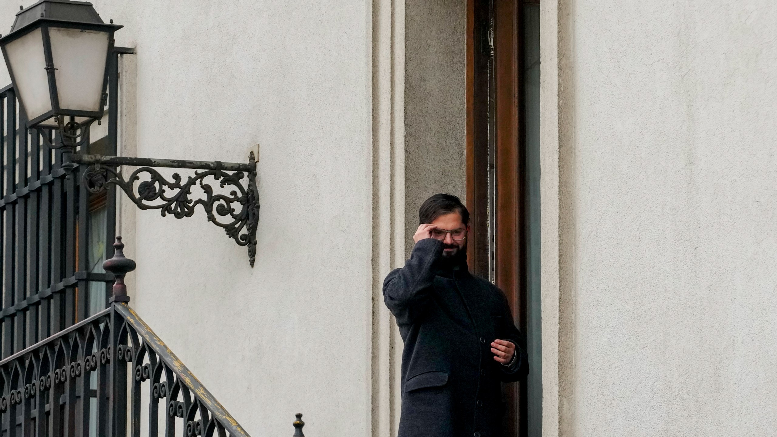 FILE - President Gabriel Boric adjusts his glasses while standing outside his office at La Moneda presidential palace, in Santiago Chile, May 29, 2024. (AP Photo/Esteban Felix, File)