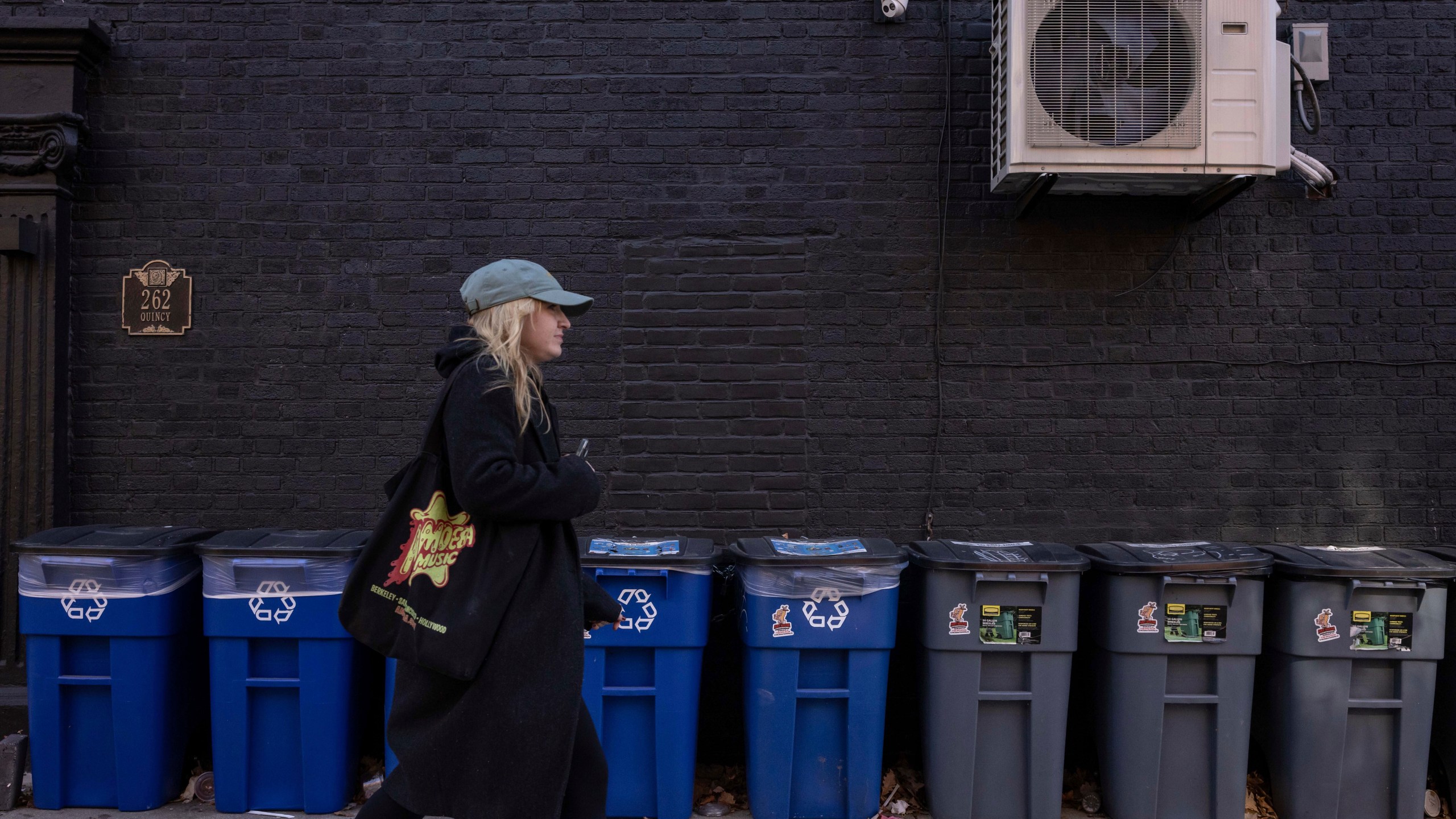 A person walks in front of trash bins, Friday, Nov. 15, 2024, in the Brooklyn borough of New York. (AP Photo/Yuki Iwamura)